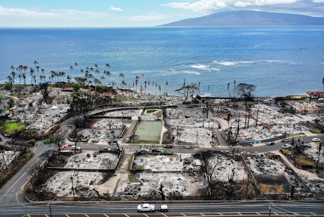 In an aerial view, a recovery vehicle drives past burned structures and cars two months after a devastating wildfire on October 9, 2023 in Lahaina, Maui, Hawaii