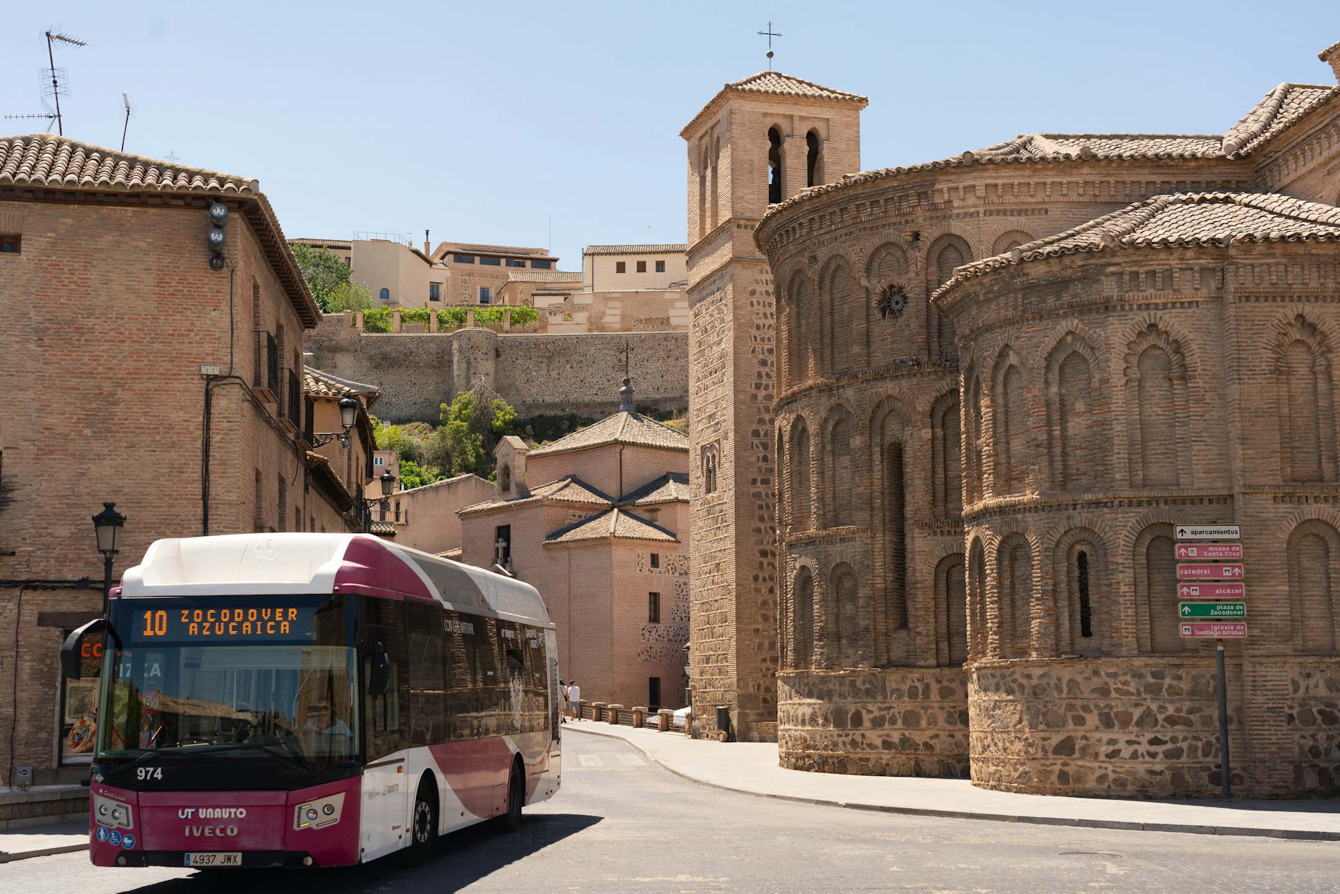 A modern public bus driving along a street lined with historic buildings in the city of Toledo in Spain