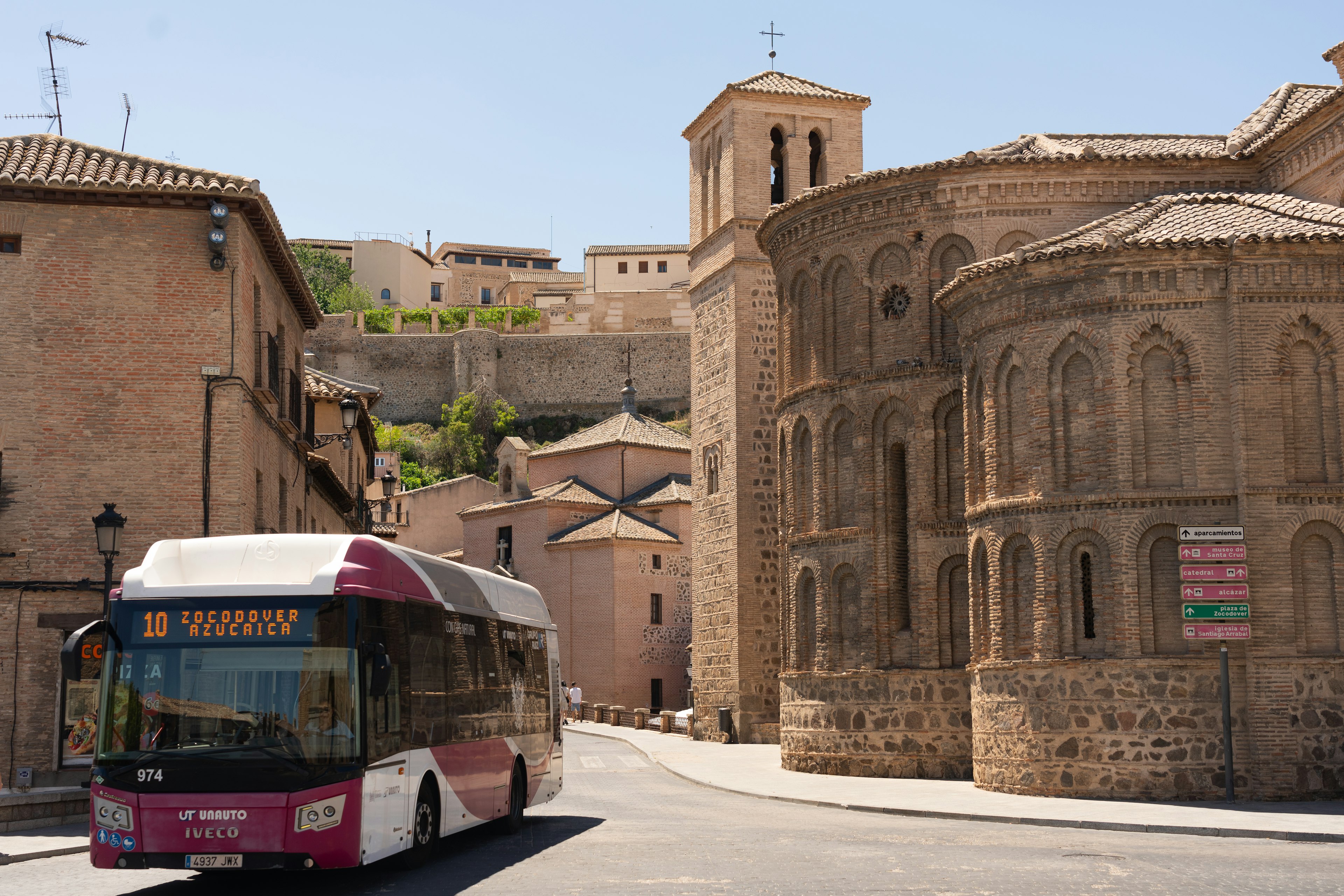 A modern public bus driving along a street lined with historic buildings in the city of Toledo in Spain