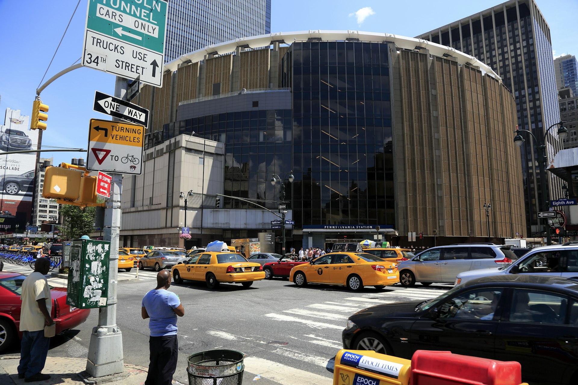 The exterior of a large entertainment complex with a curved facade. Many yellow taxis are passing in the street 