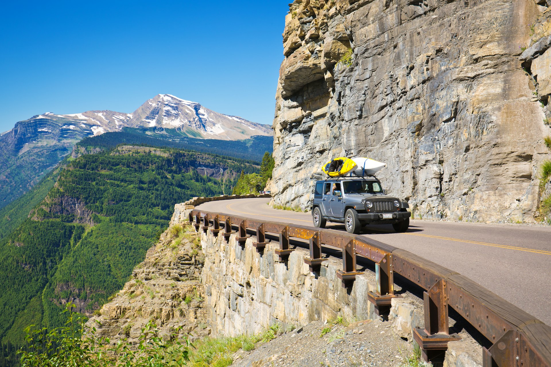 A jeep with kayaks on its roof drives along Going-to-the-Sun Rd, Glacier National Park, Montana, USA