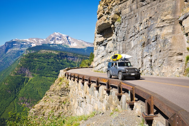 A jeep with kayaks on its roof drives along Going-to-the-Sun Rd, Glacier National Park, Montana, USA