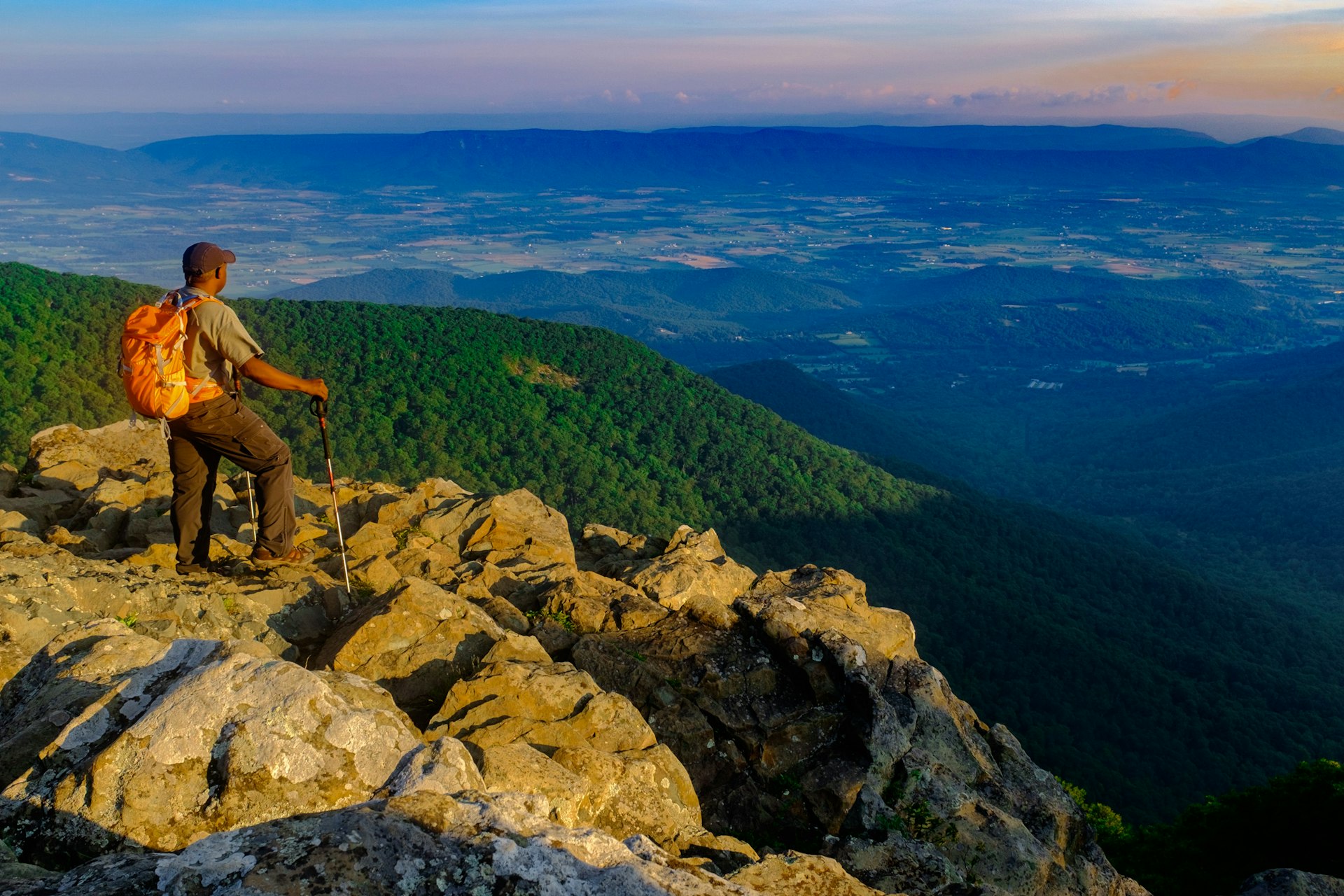 A hiker stands at a viewpoint looking out over a vast green valley