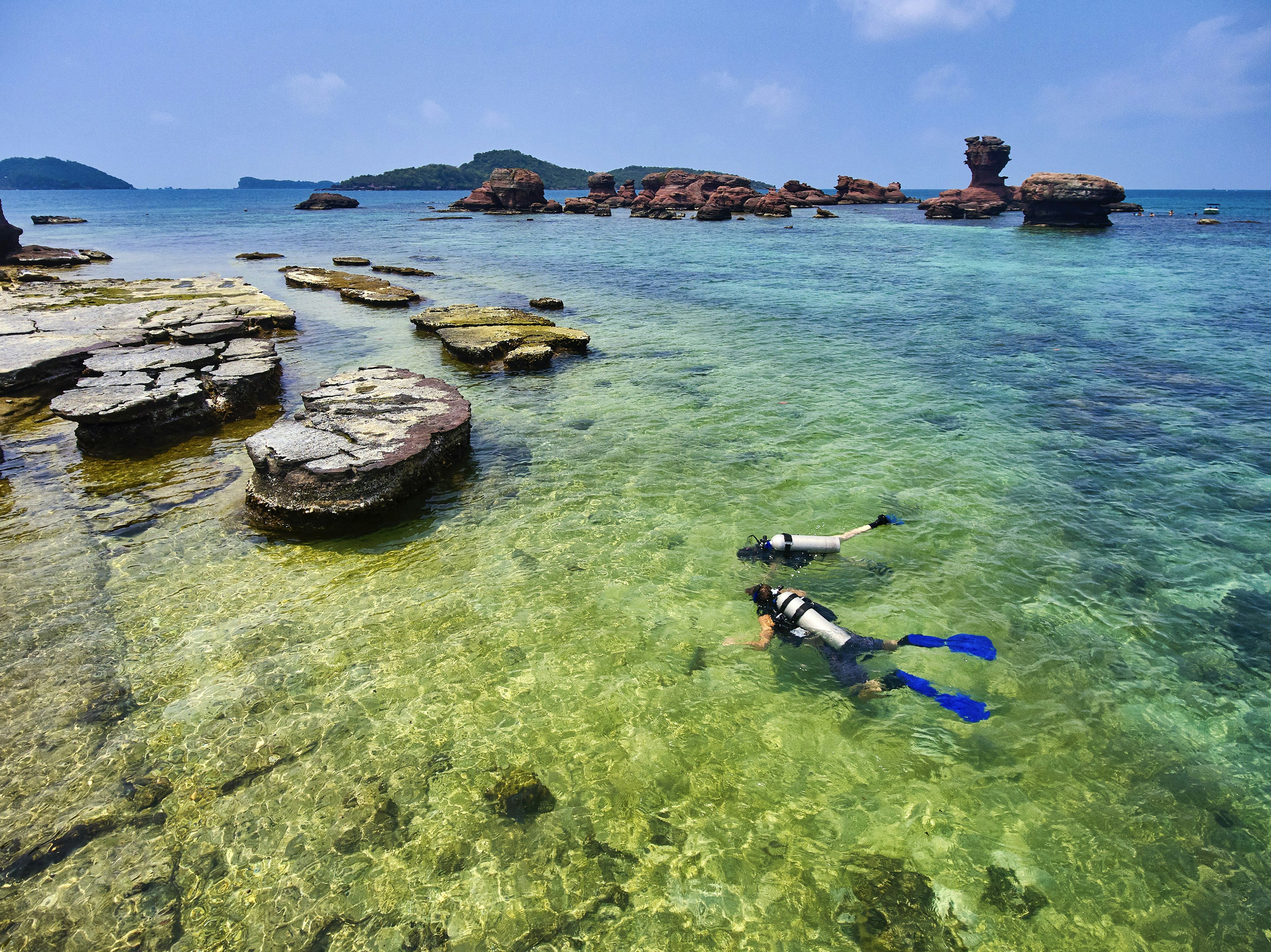 Two divers swim among rocks in clear water on Hom Gam Ghi in Phu Quoc