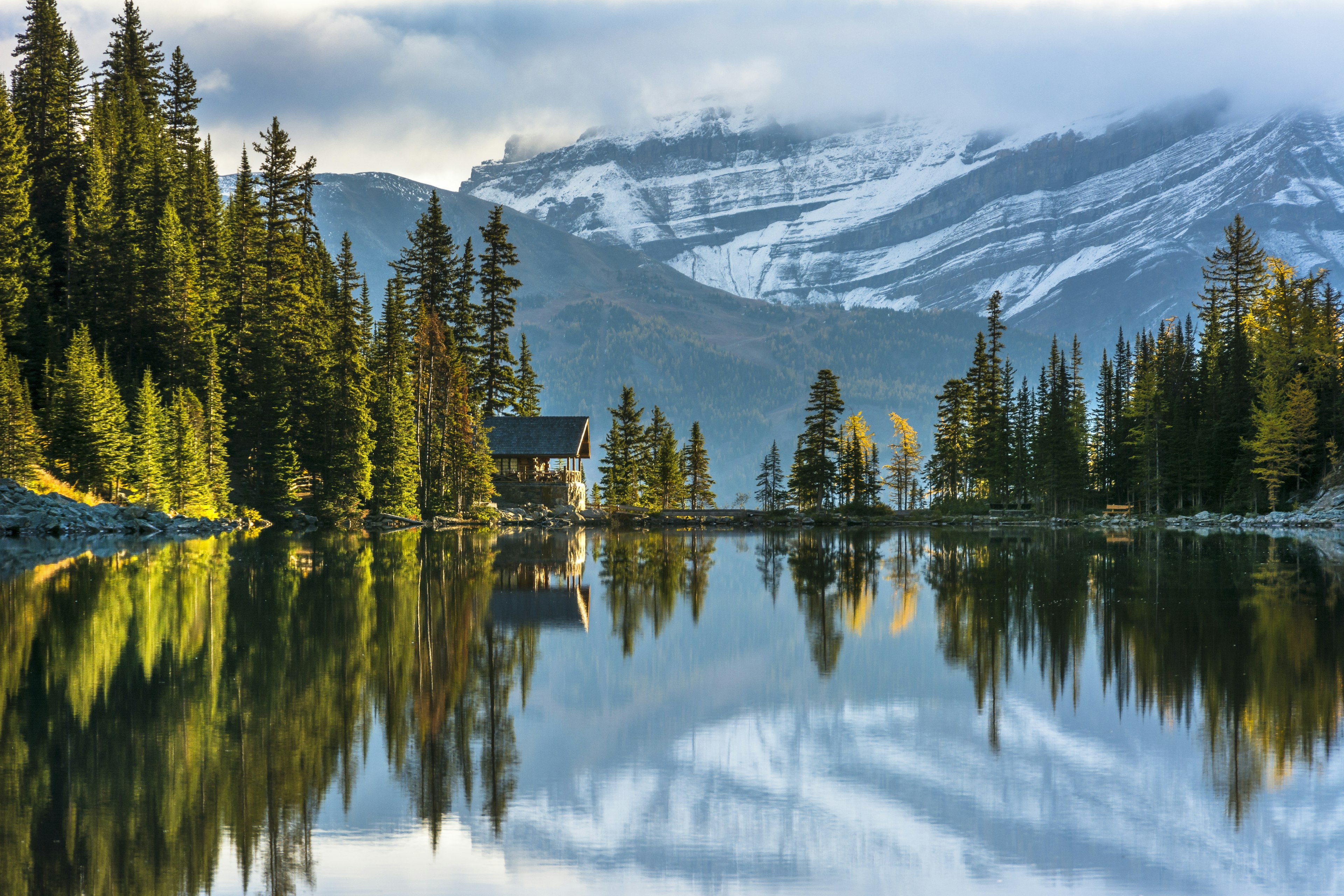 Mountains reflected in a lake with a small wooden structure tucked in the cliffs