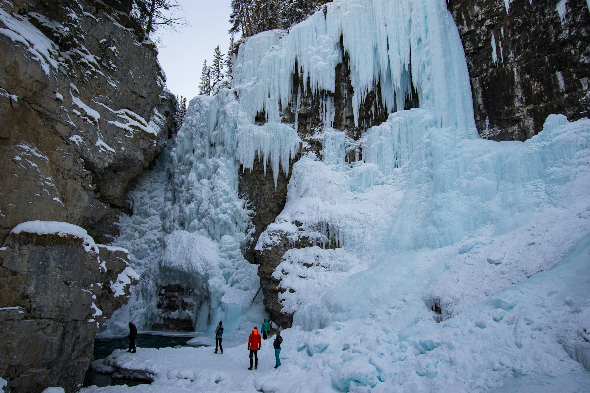 Hikers stand at the foot of a frozen waterfall