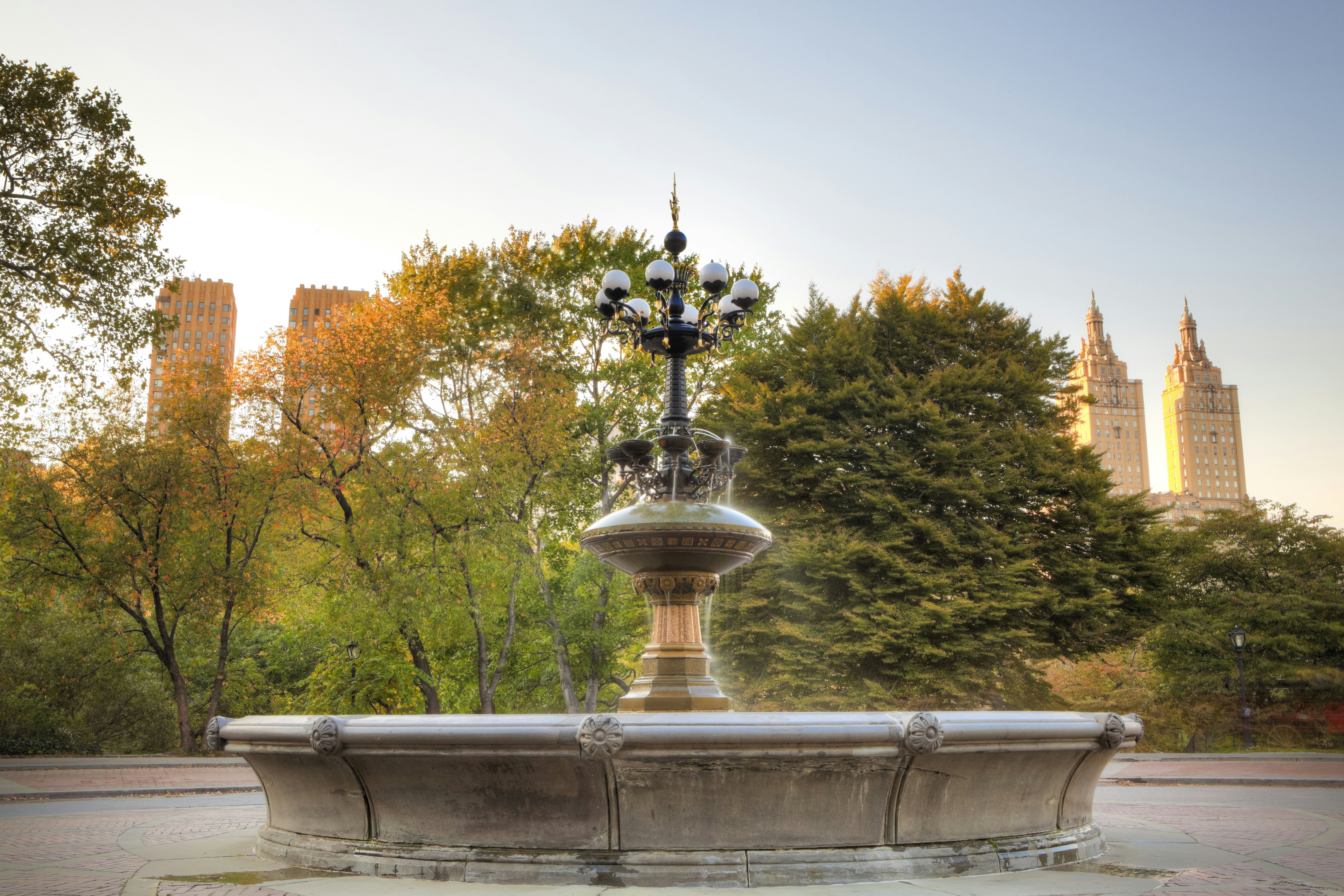 A fountain in parkland with skyscrapers looping above