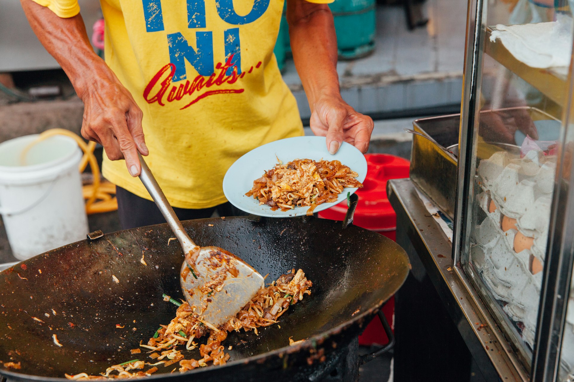 A hawker prepares a noodle dish in a wok at a street food market