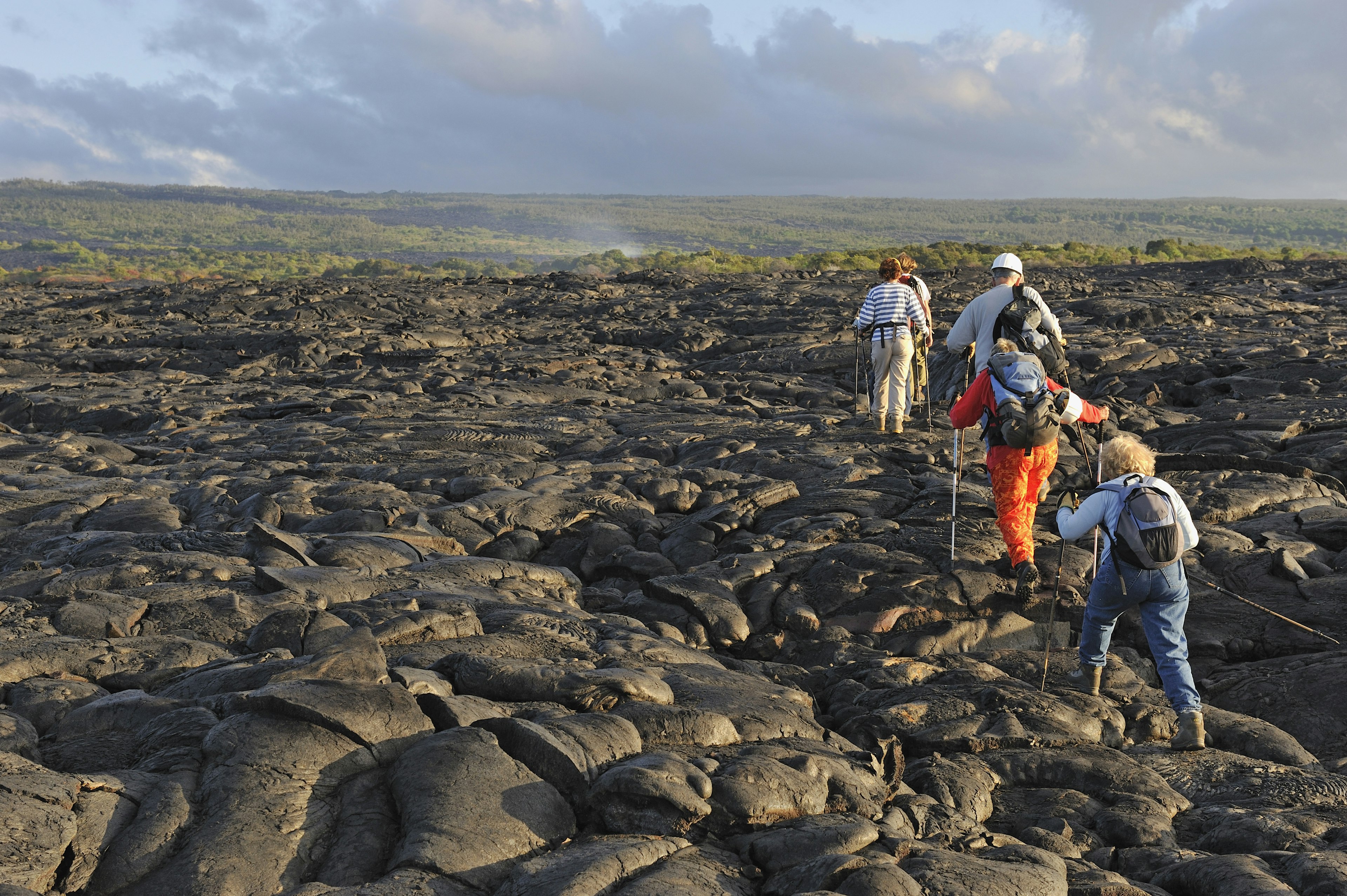 Group of hikers walking on cooled lava flow of black rock