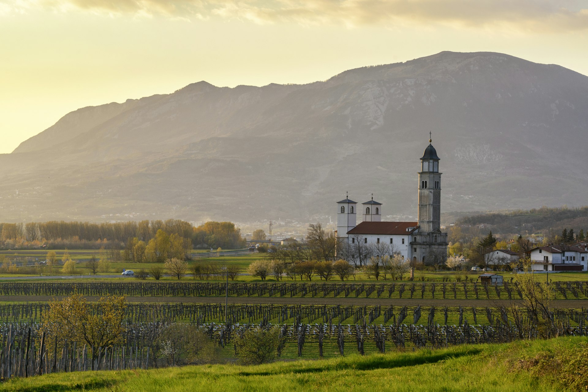 A church stands among vineyards and mountains in a lush Slovenian valley. 