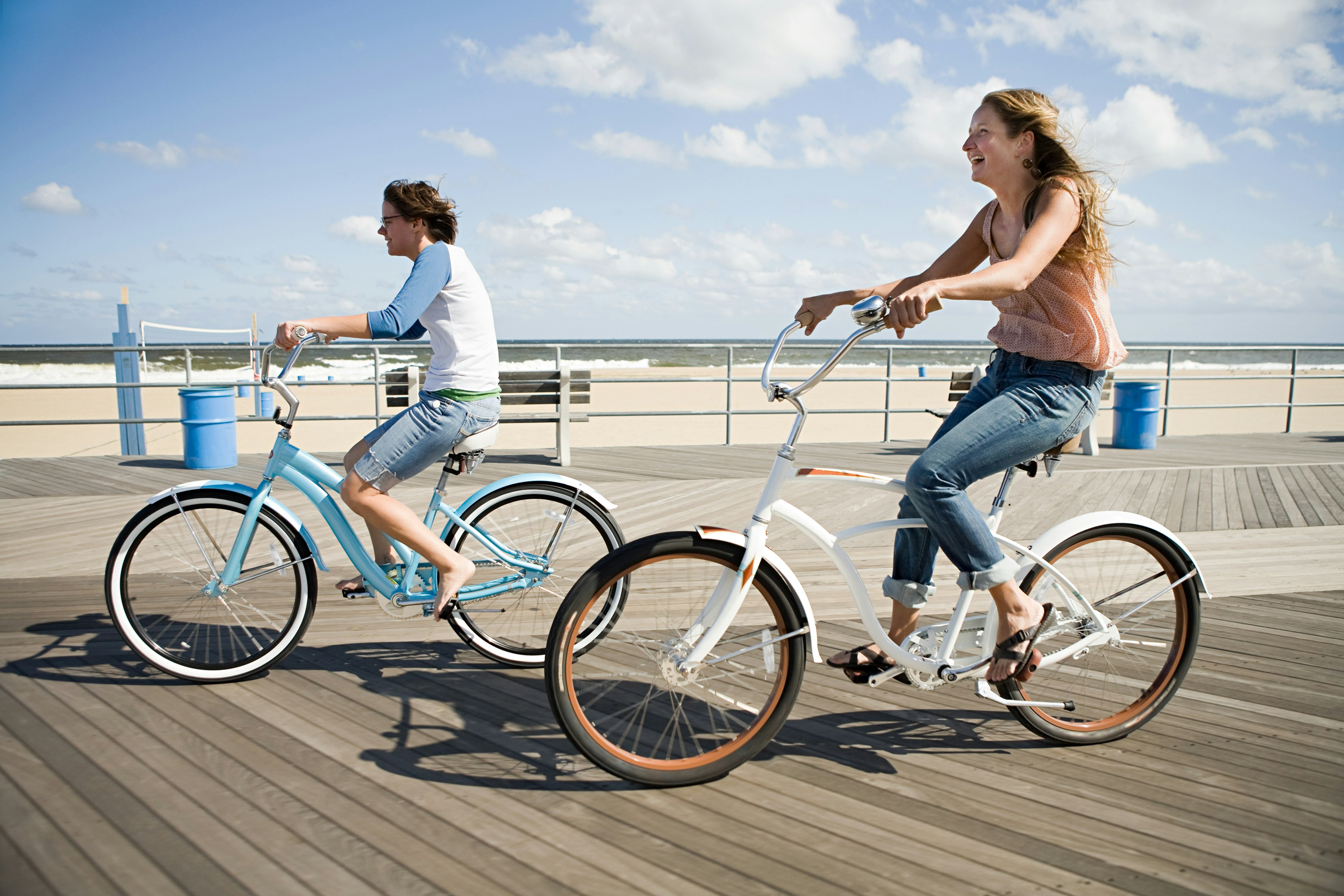 Two white people riding bikes on boardwalk backed by a large empty sandy beach