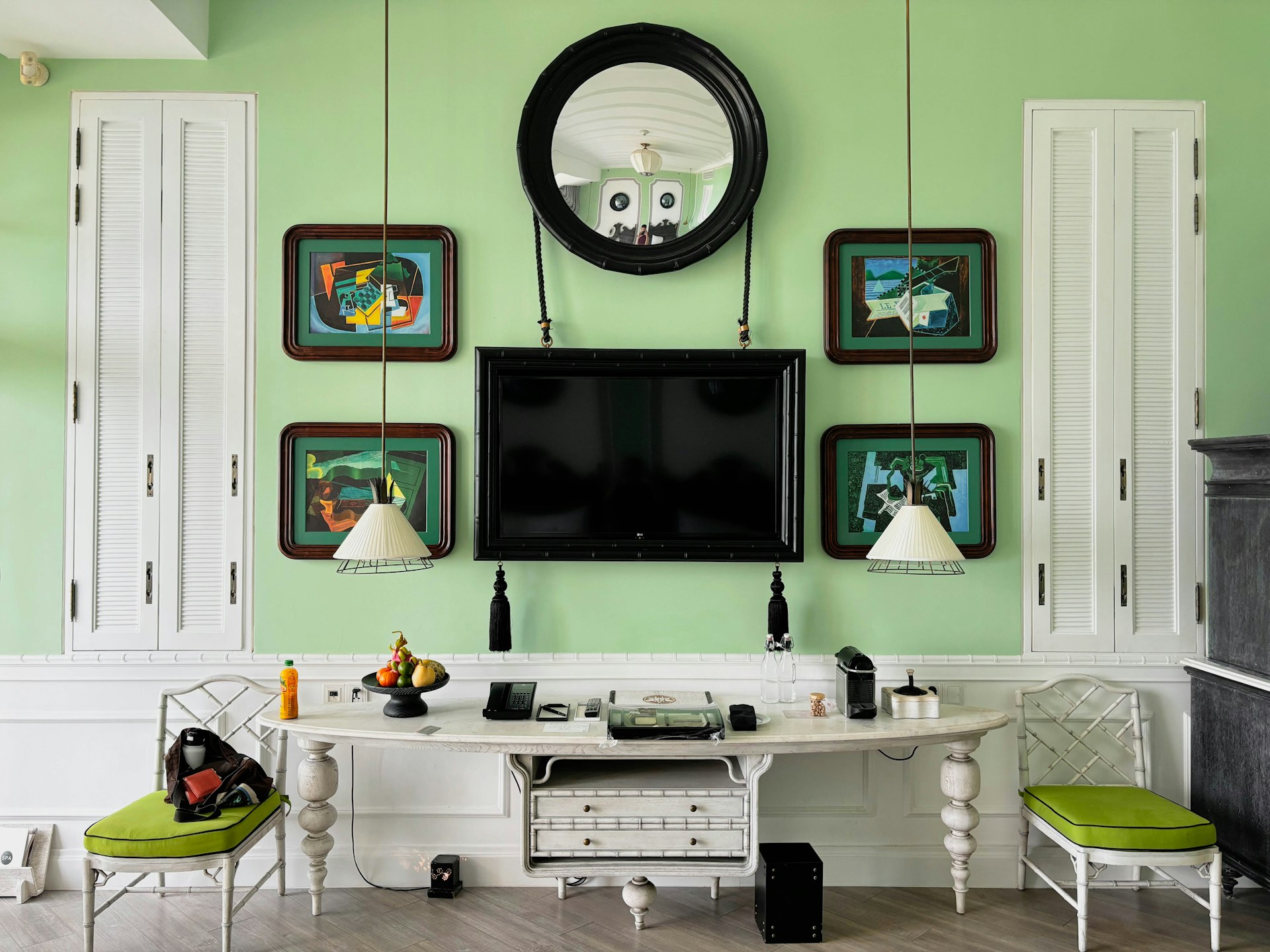 A TV and paintings hang on a mint-painted wall above a white table in a stylish hotel bedroom