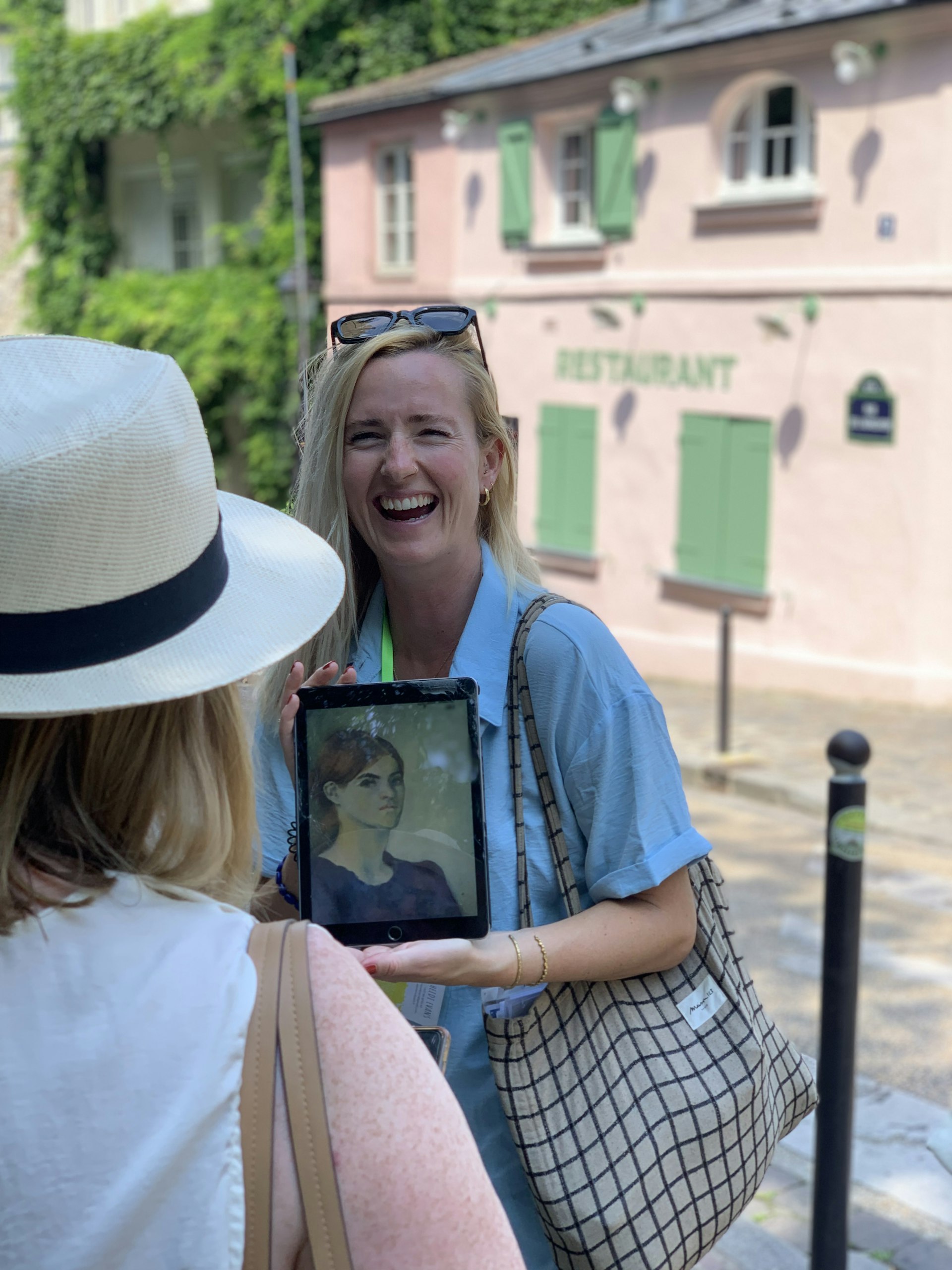A tour guide smiles as she tells a story about the woman in the picture she is holding