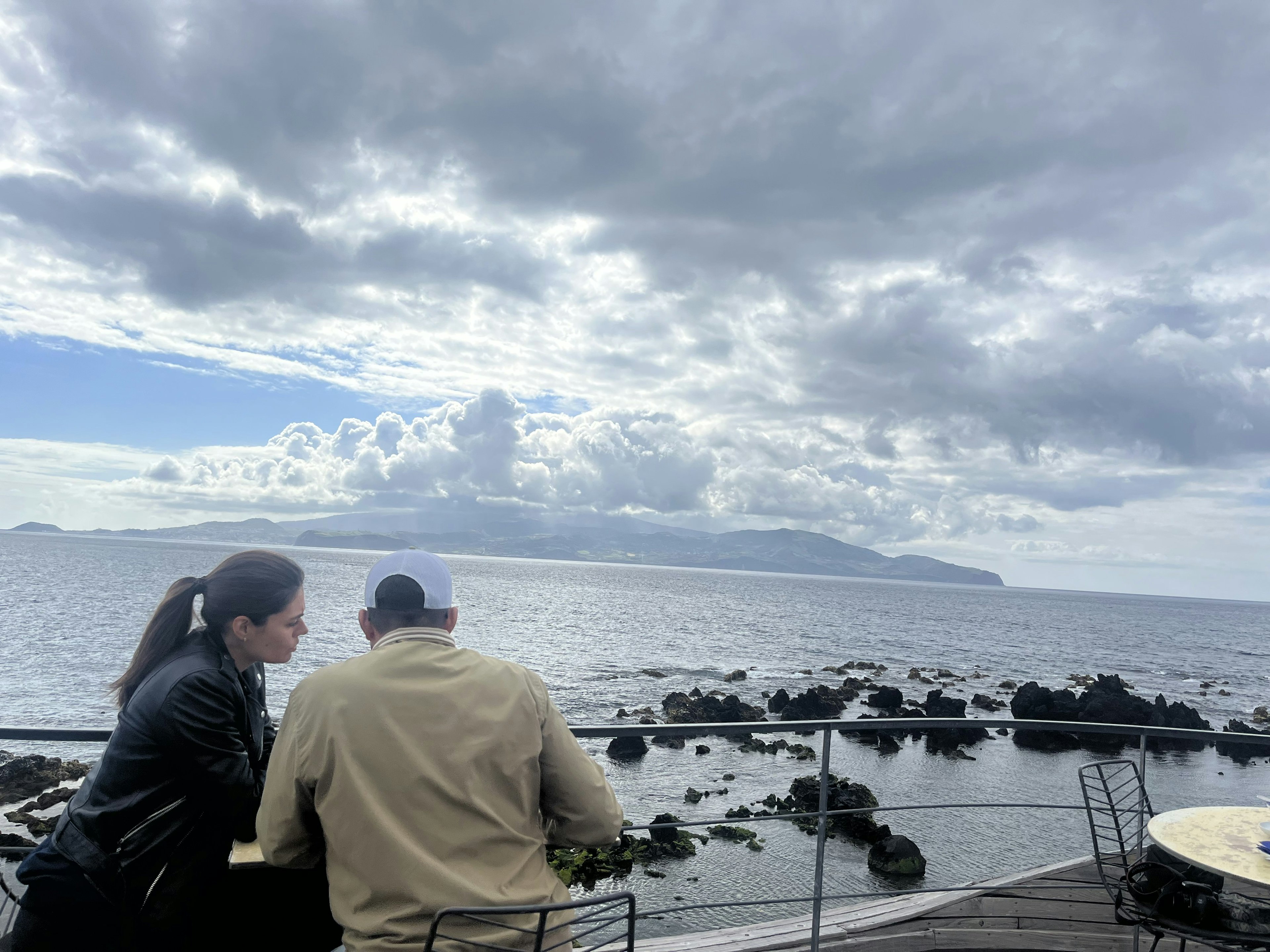 A couple sit at a table looking out to sea