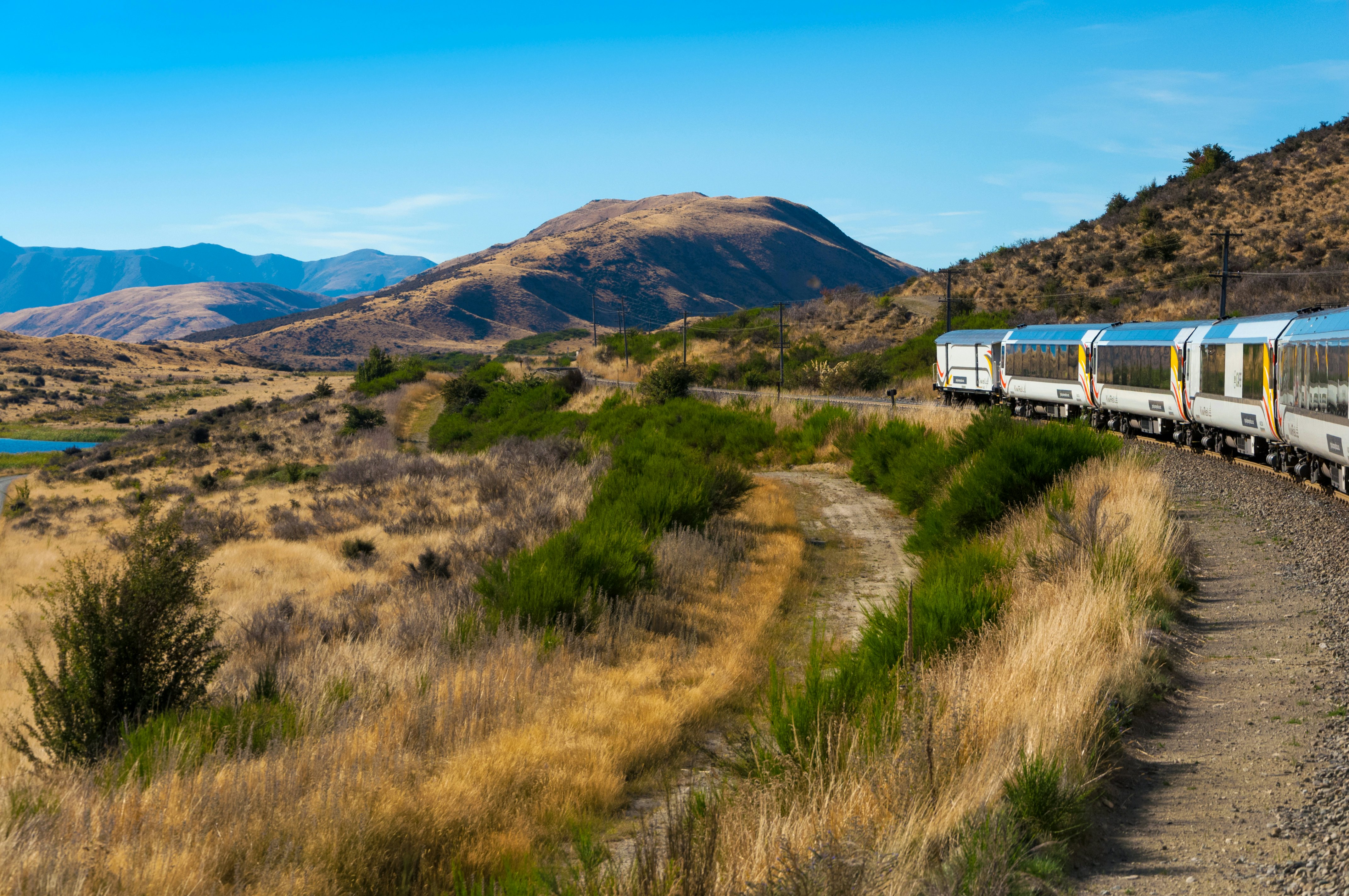 A train curves around a grassy meadow in a mountainous region.