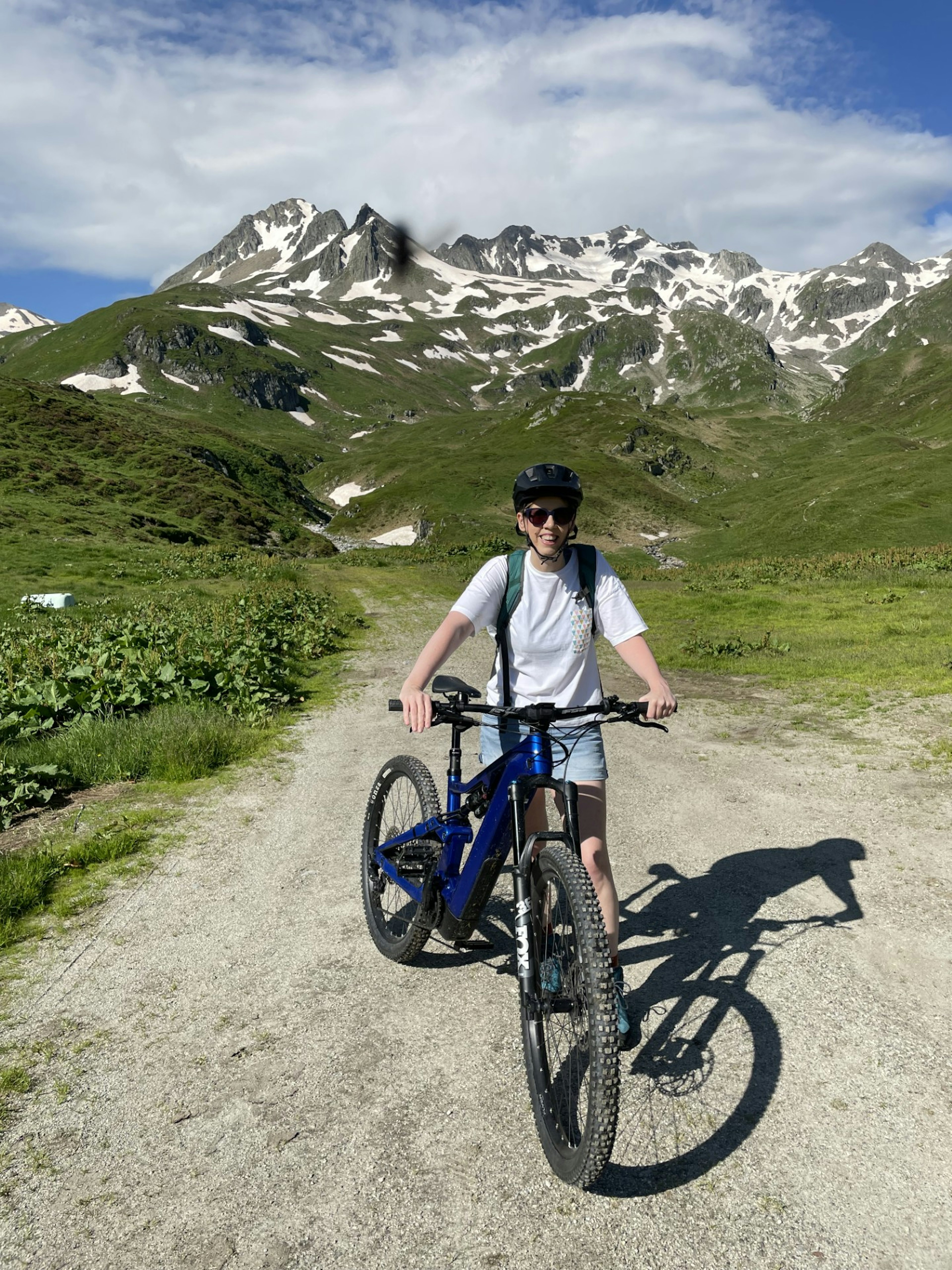 A woman stands next to a bike in an alpine meadow