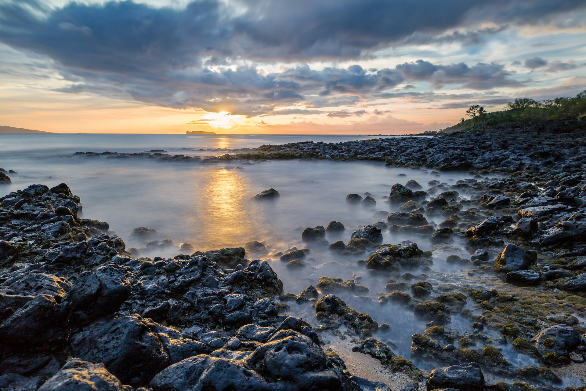 Waves smash against volcanic rocks as the sun sets out at sea