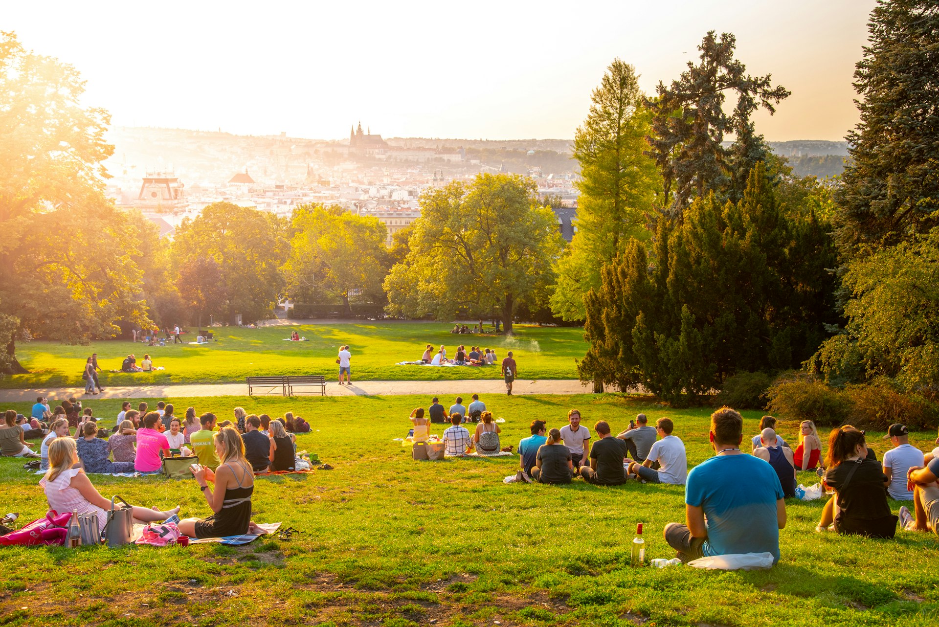  Sunset in Rieger Gardens, Riegrovy sady, in Prague. Many people sitting in the grass and enjoying sunny summer evening and lookout of Prague historical city