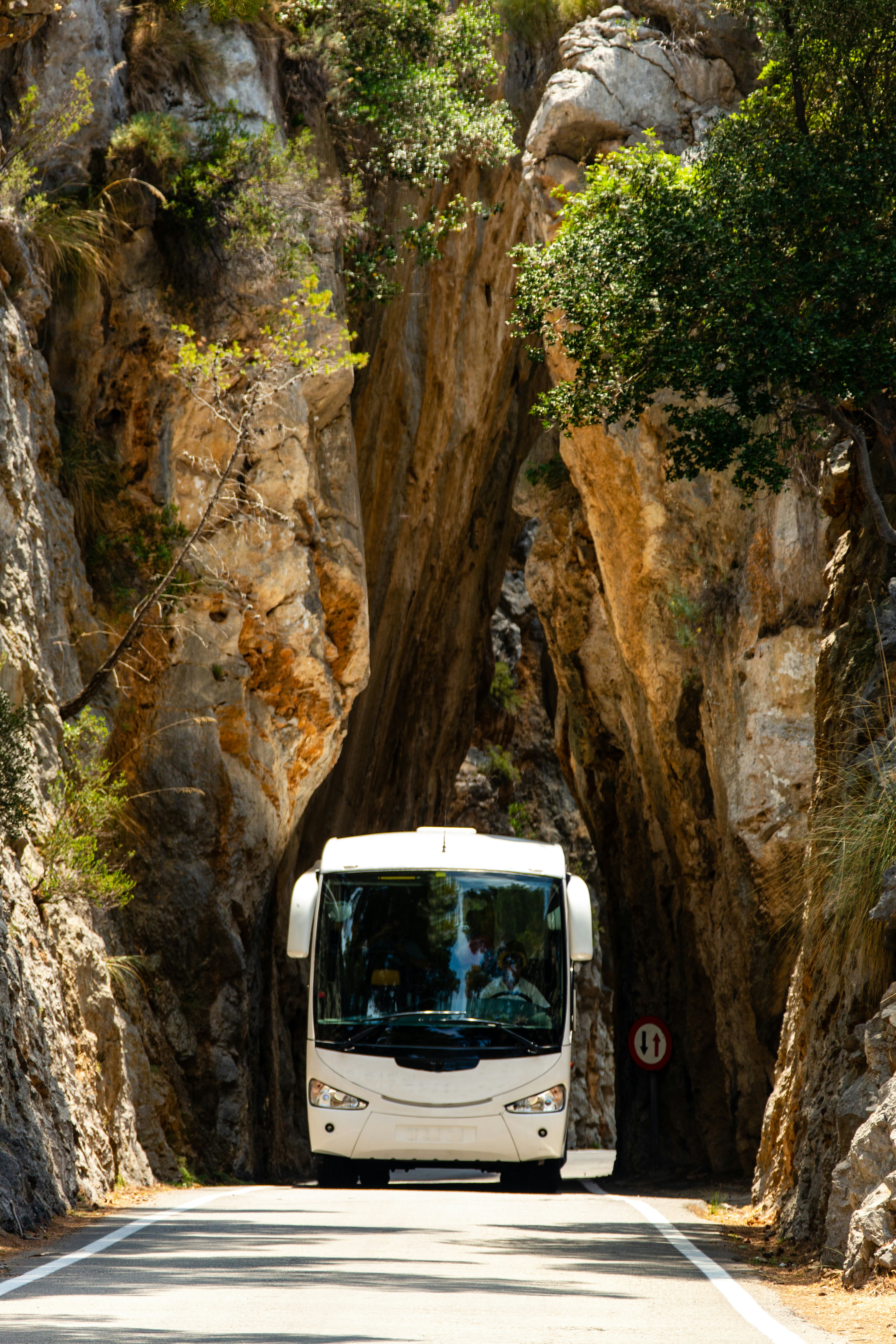 A coach drives through a very narrow natural rock arch on a mountain road in Mallorca, Spain