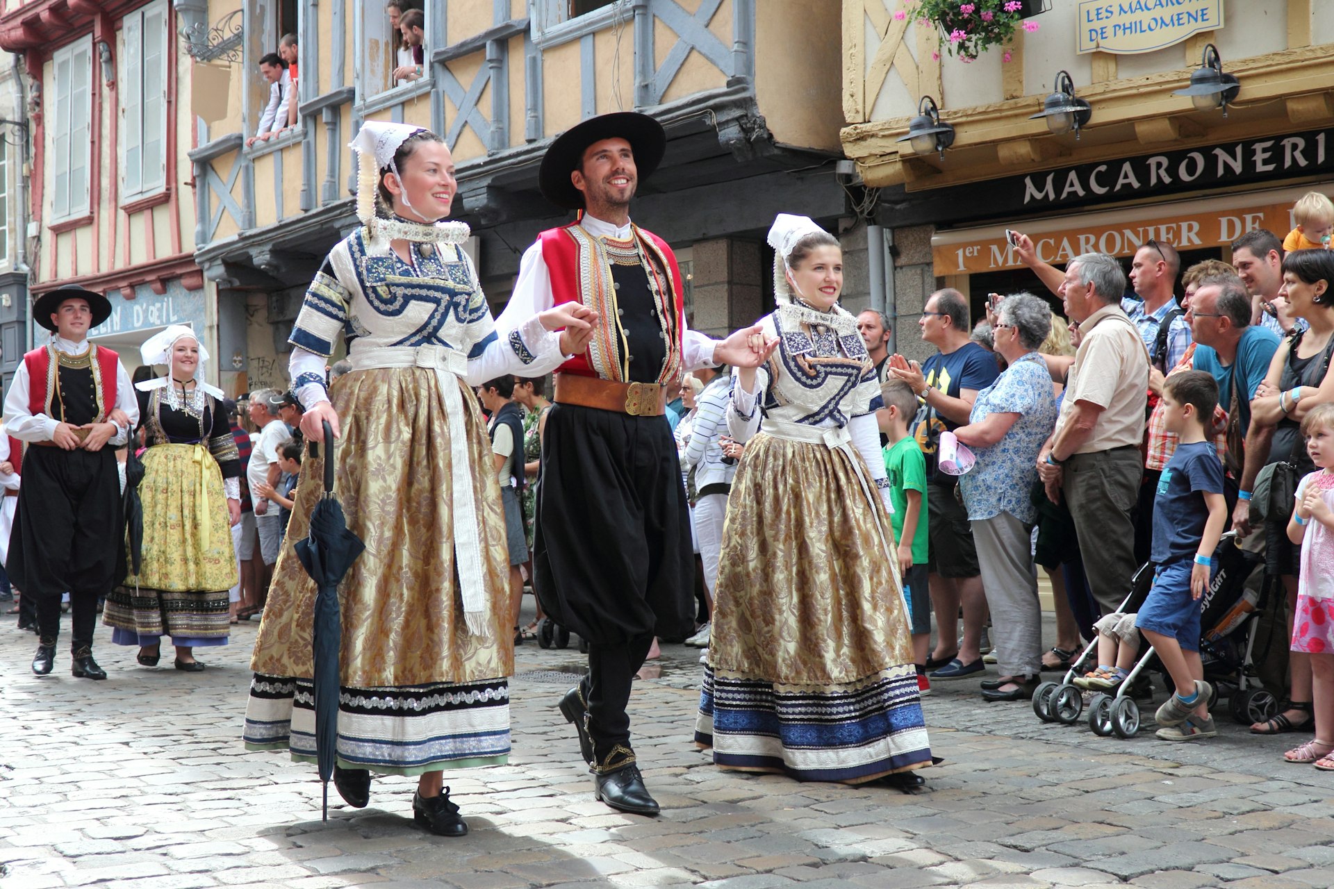 A man and two women in traditional dress smile as they parade down the street during a festival