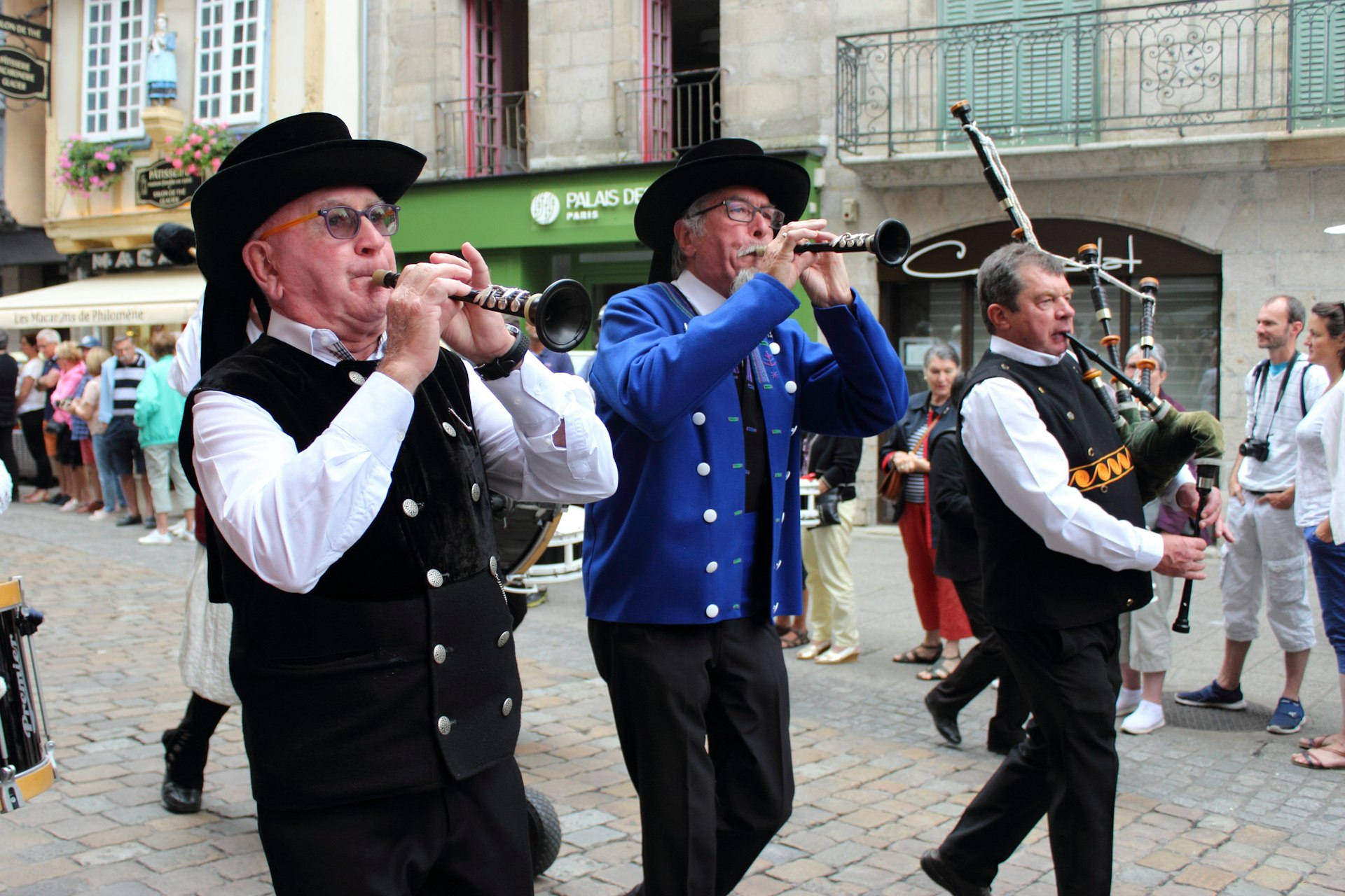 Three men play wind instruments as they walk down a street at a traditional arts festival