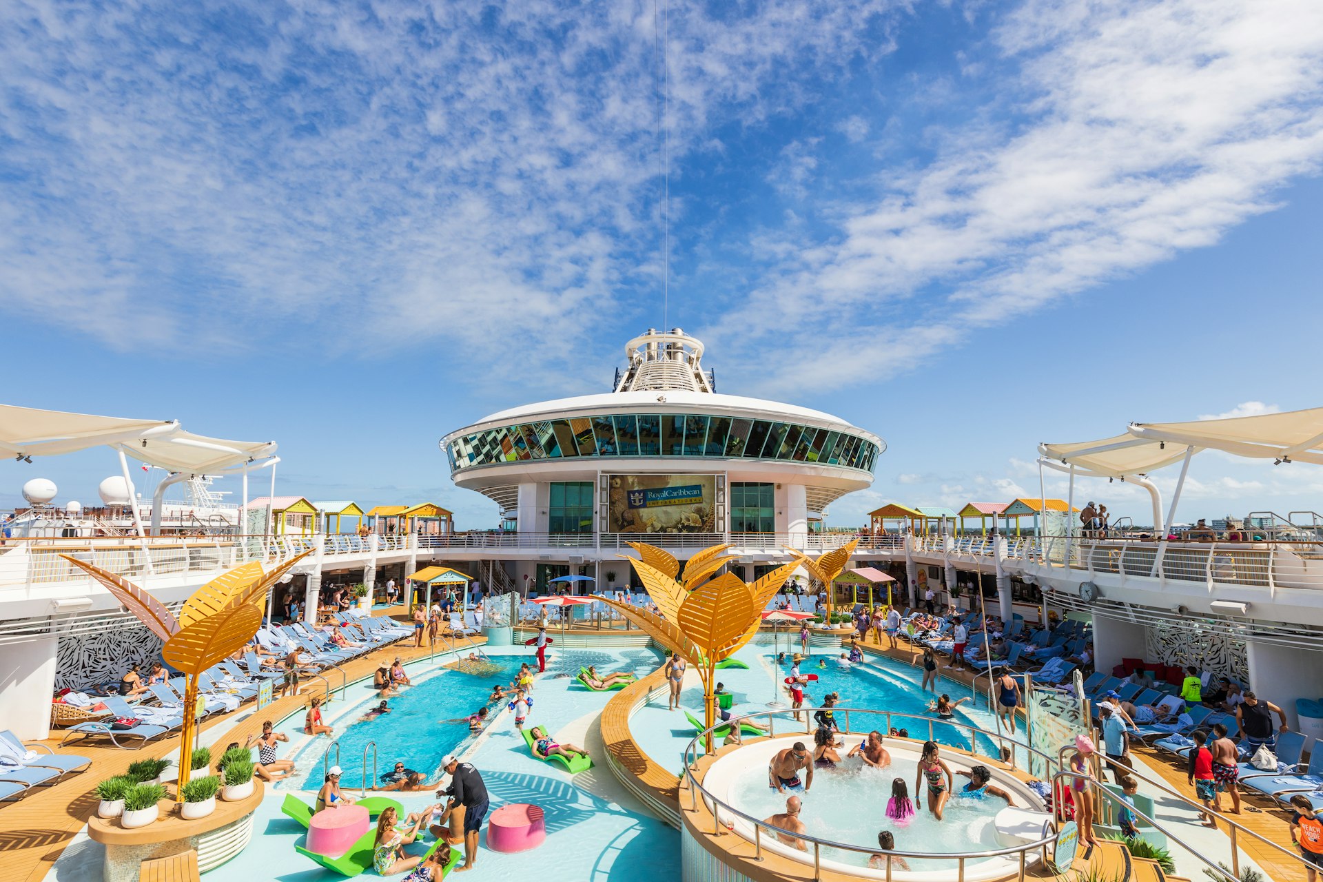 The top of a Royal Caribbean cruise ship with a balcony looking down over a pool with people and lounge chairs.;