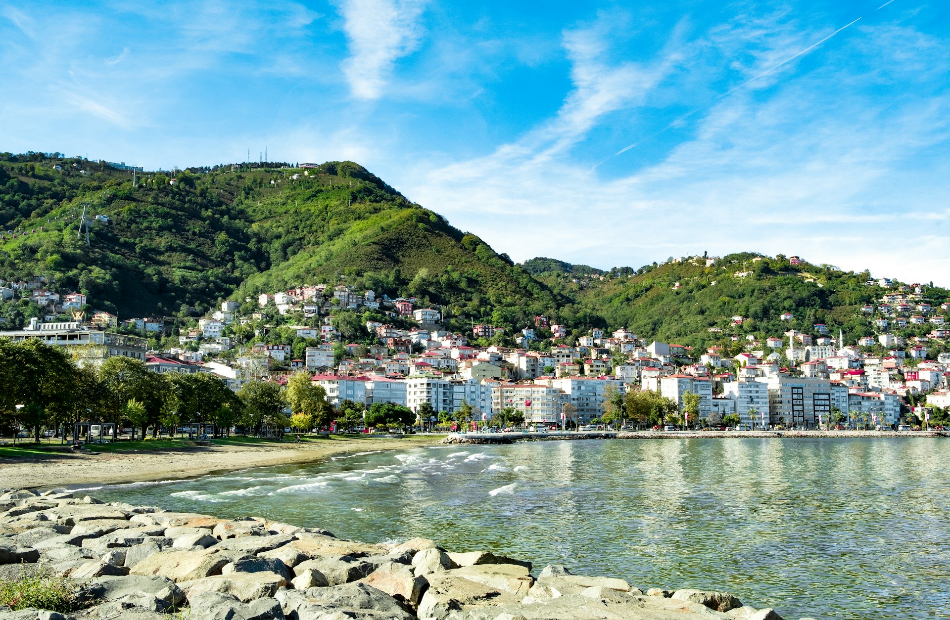 The rocky shore of a seaside town backed by buildings built into the steep hillside