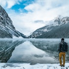 Male hiker enjoys the nature landscape outdoors with backpack at iconic Lake Louise in Banff National Park, Alberta, Canada. Majestic rocky peaks covered with snow reflect on the calm water surface. © Alexander_Magnum / Shutterstock