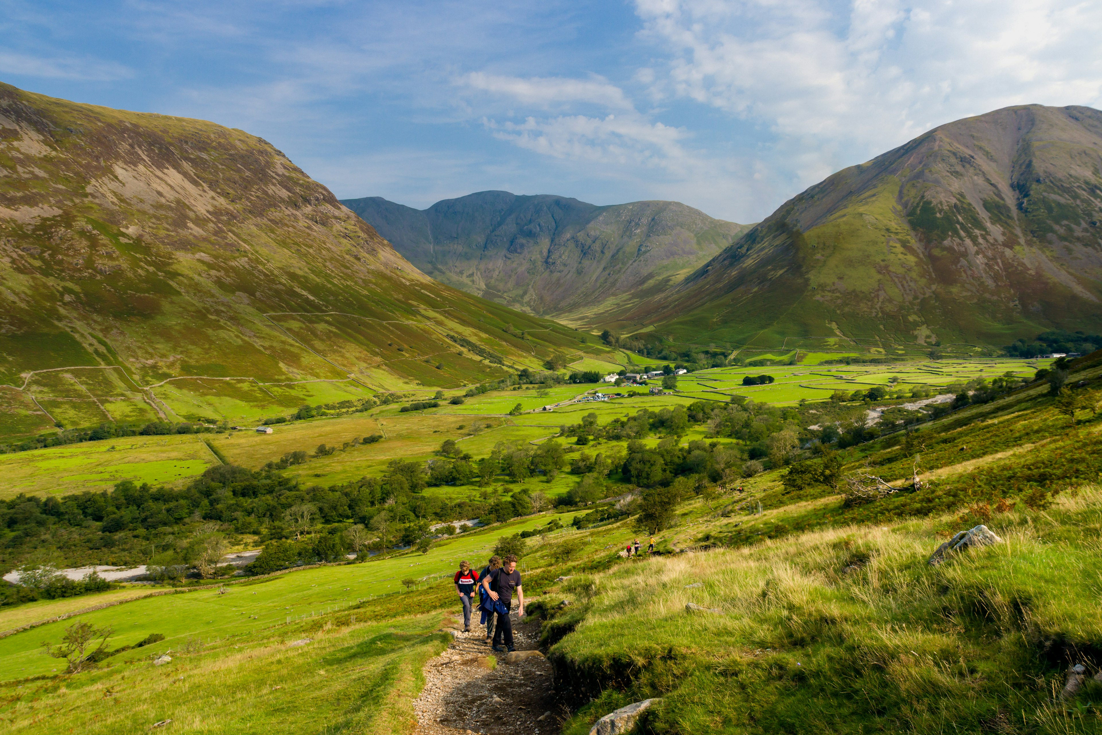 Hikers start making their way up a steep gravel pathway with beautiful green hills rolling behind them