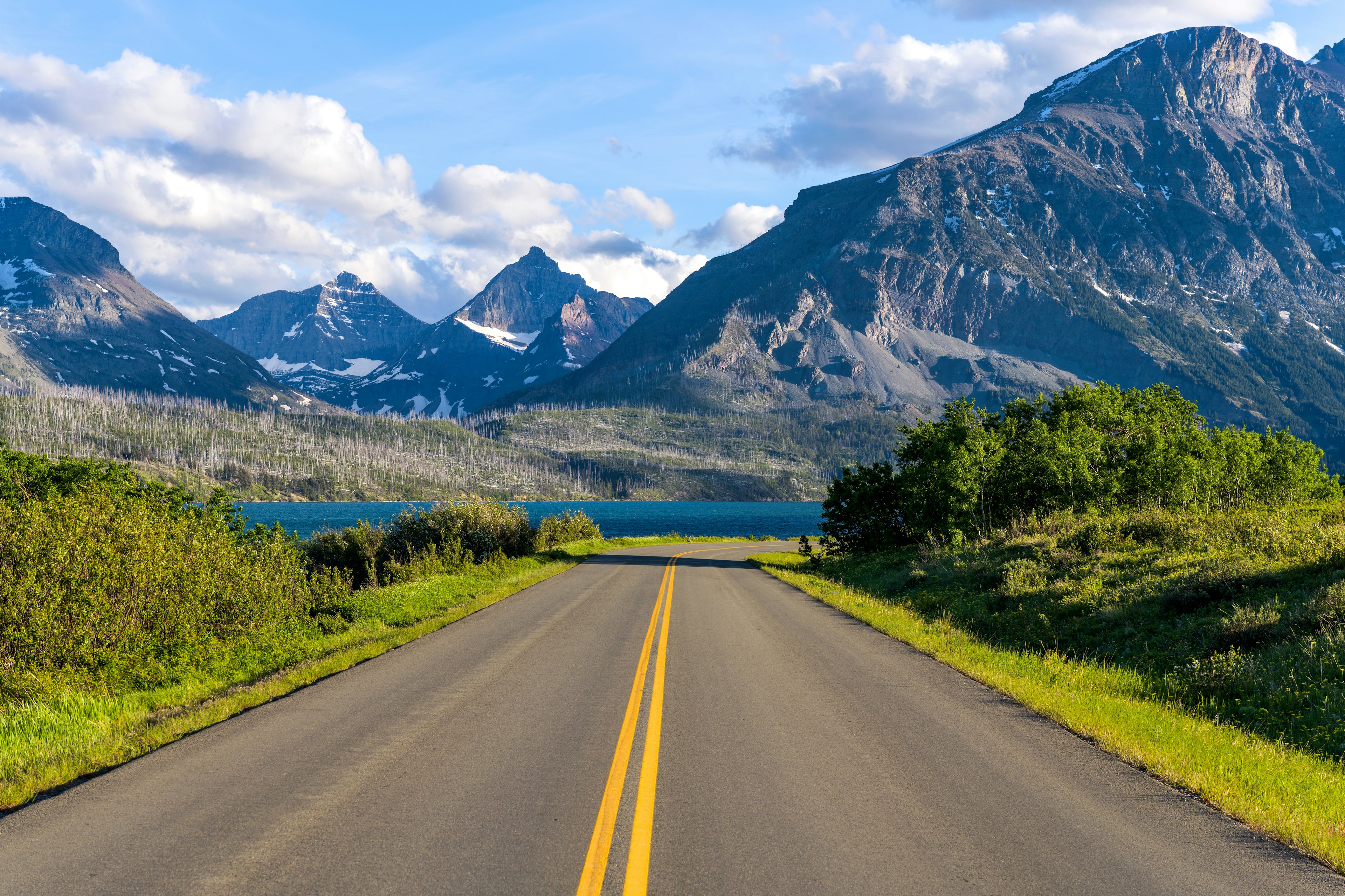 A road in a mountainous area descends towards a lake