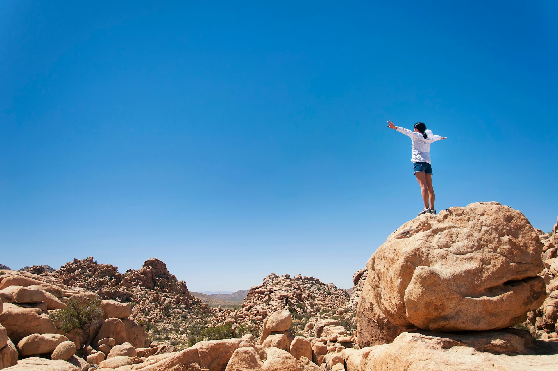 A woman standing on a large boulder overlooking Hidden Valley Trail, Joshua Tree National Park, California, USA 