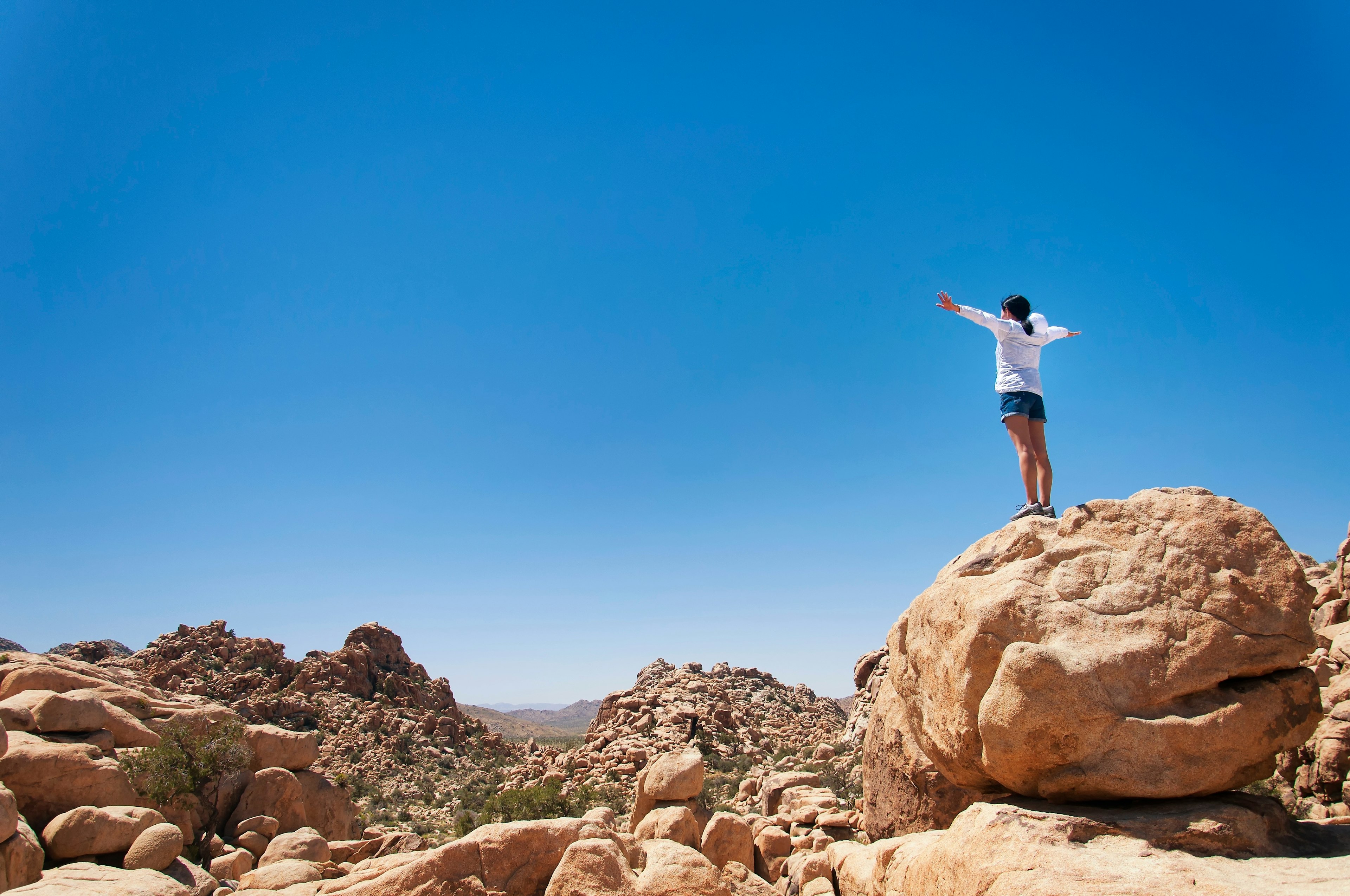 A woman standing on a large boulder overlooking Hidden Valley Trail, Joshua Tree National Park, California, USA