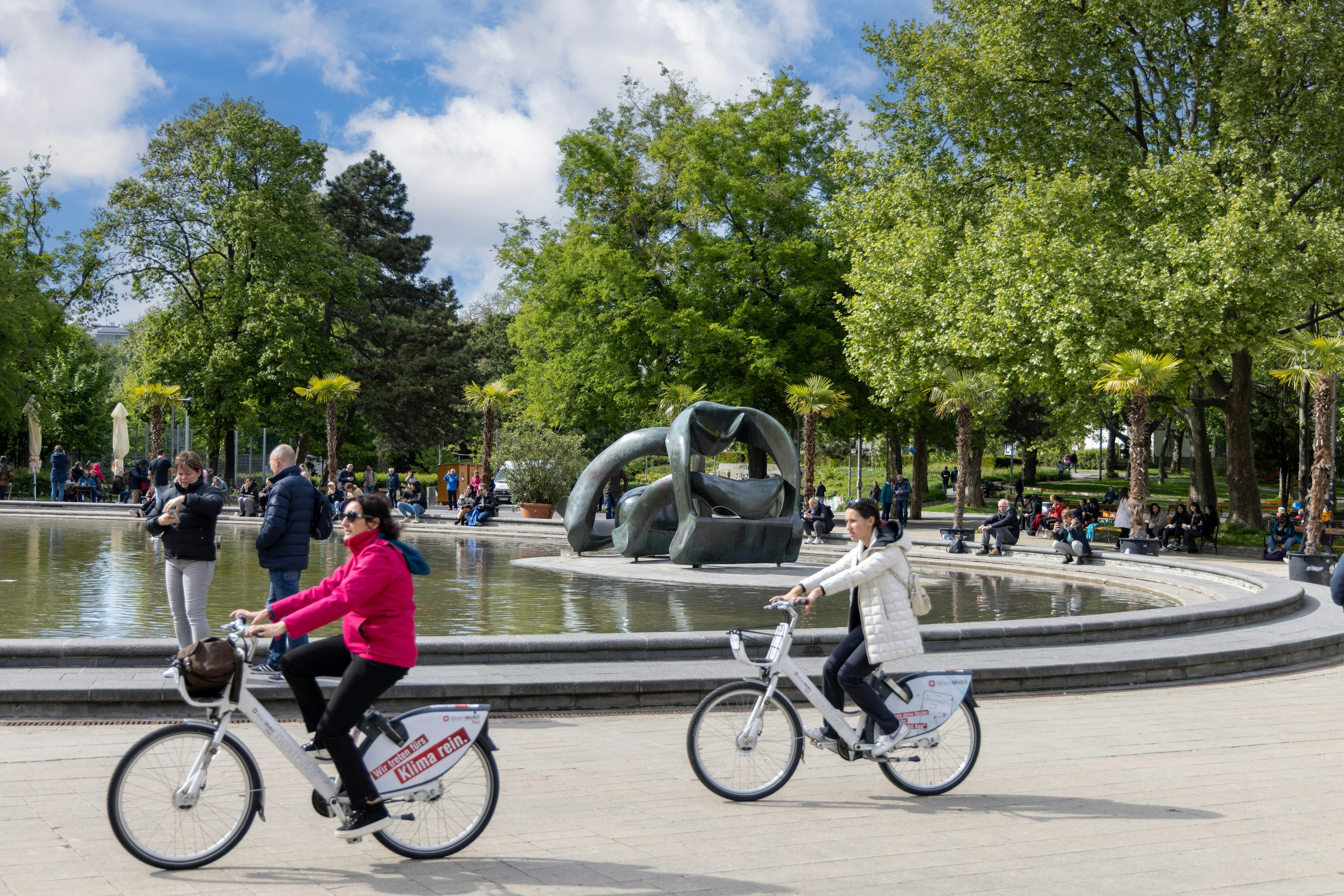 : People ride bikes and relax in the park in the Karlsplatz in front of Church of St. Charles (Karlskirche)