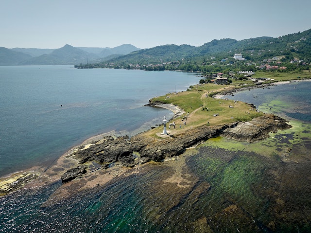 A narrow peninsula, with a white lighthouse at its tip, stretches out to sea