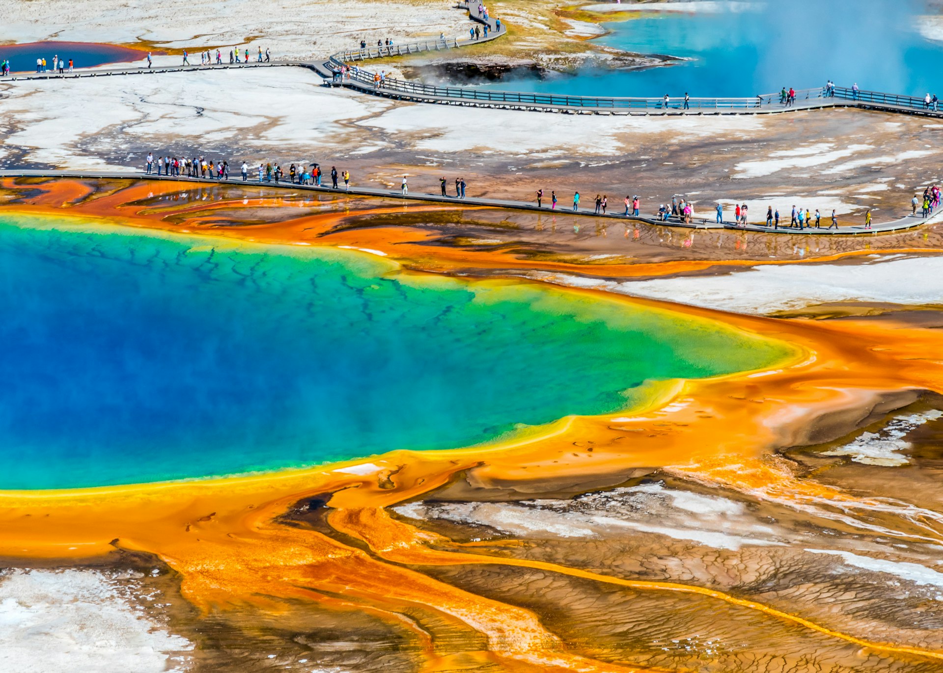 People follow boardwalks around colorful geothermal lakes