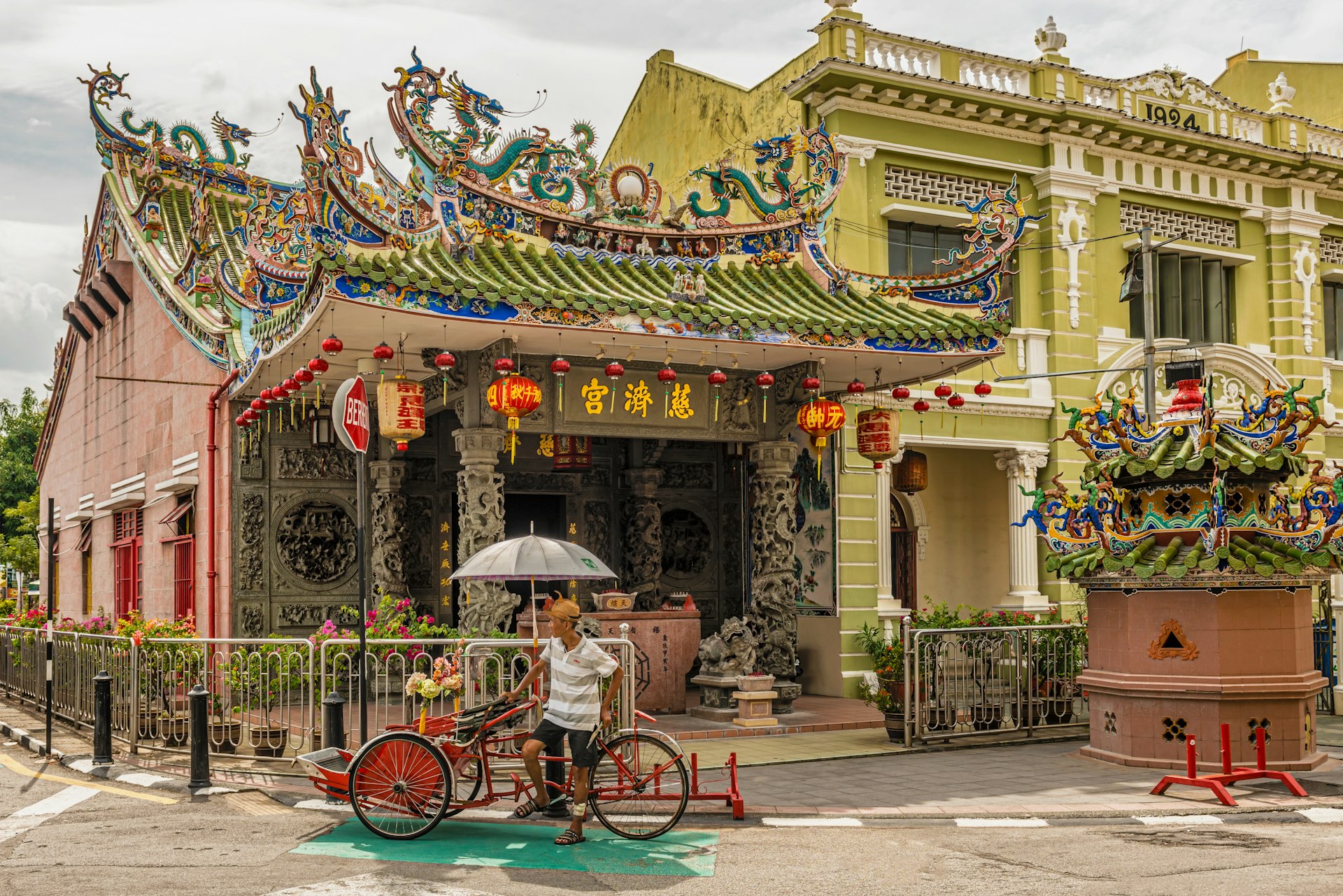 A man stands by a rickshaw outside a temple with Chinese-style red lanterns 