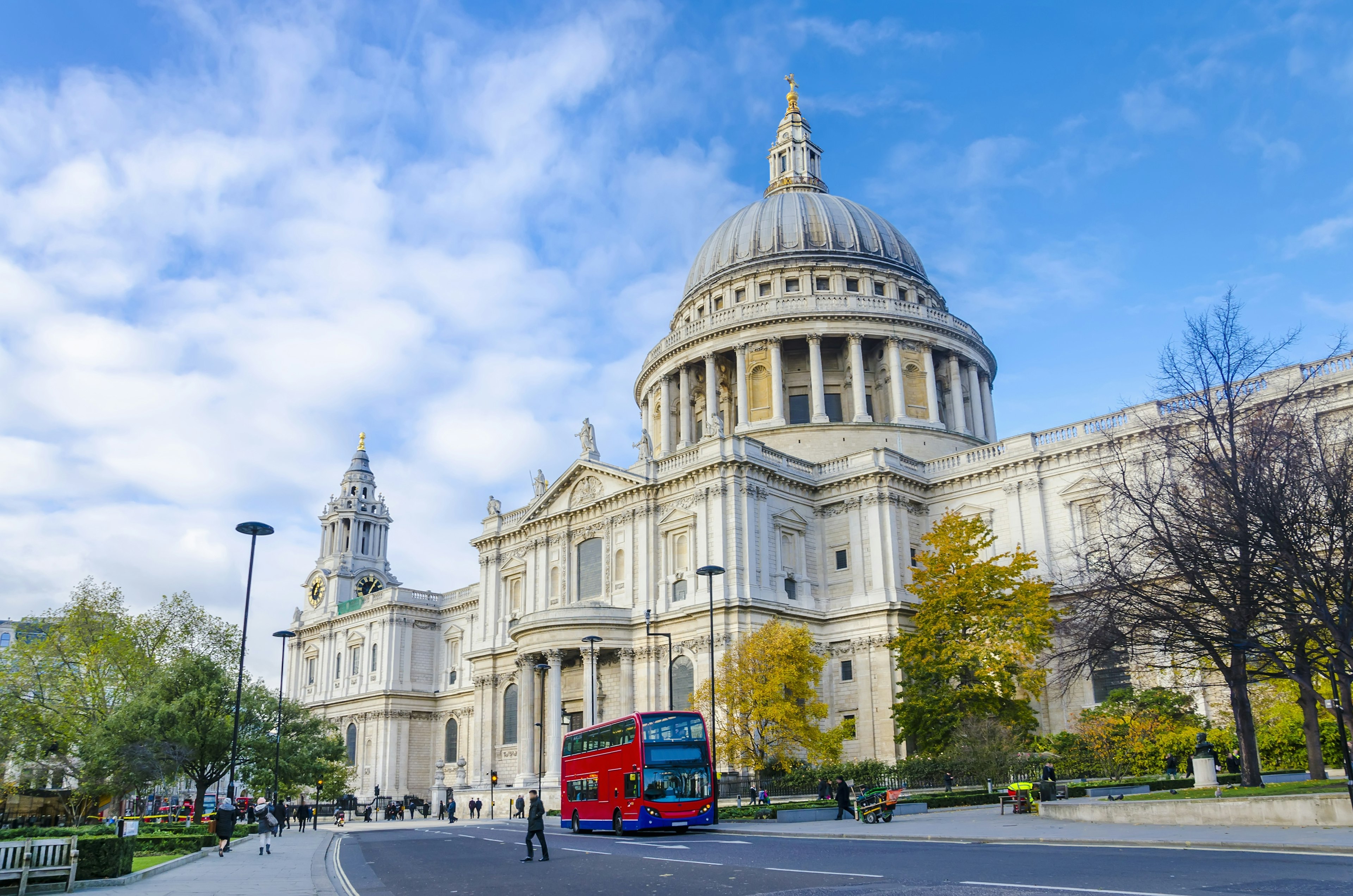 A red double-decker bus passes in front of a large domed cathedral