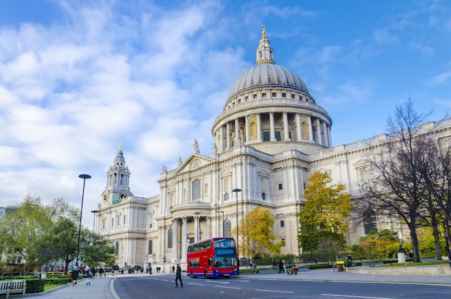 A red double-decker bus passes in front of a large domed cathedral