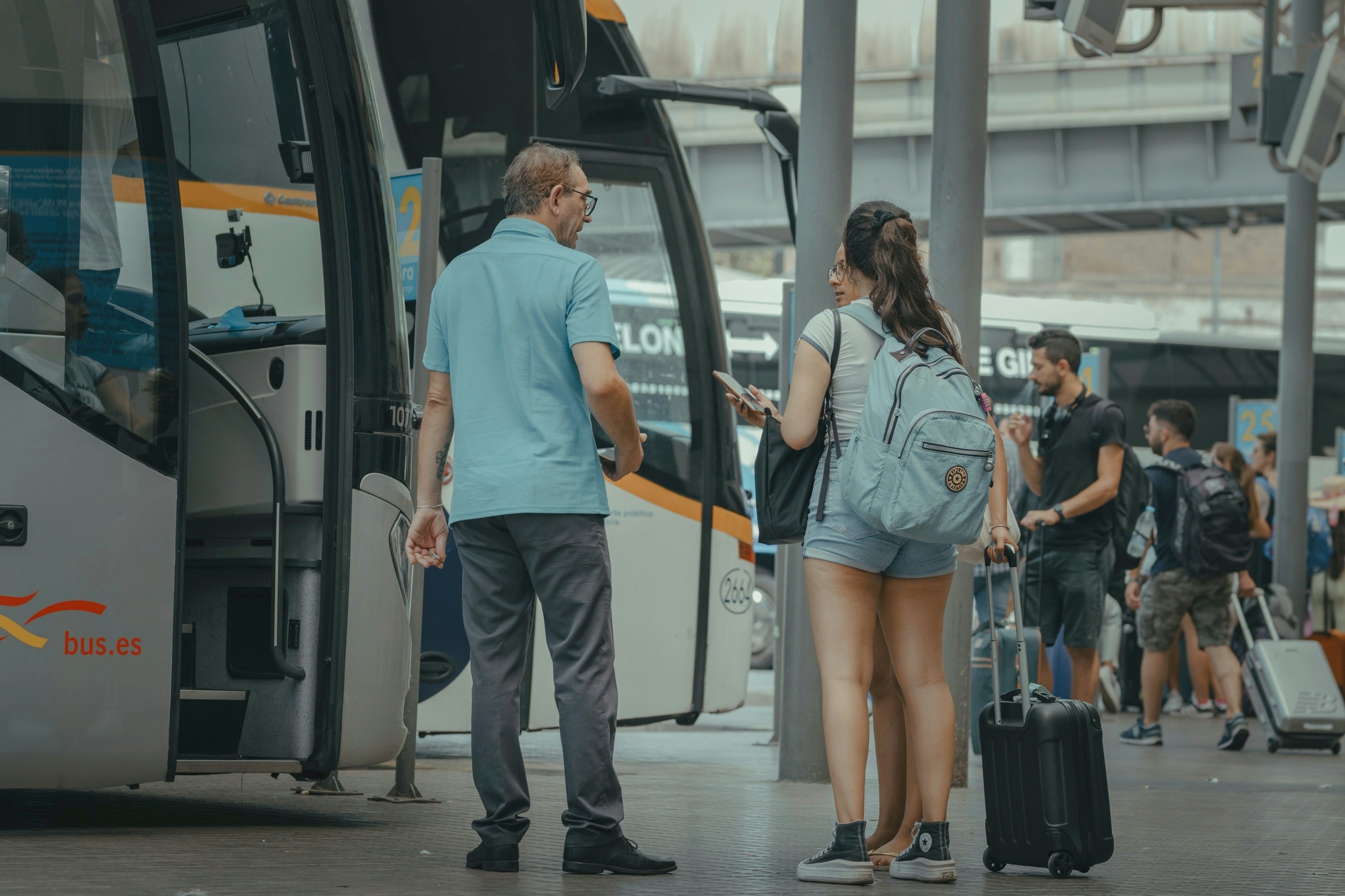 A bus driver talks to two passengers as they wait to boad a coach at a bus station in Barcelona, Spain