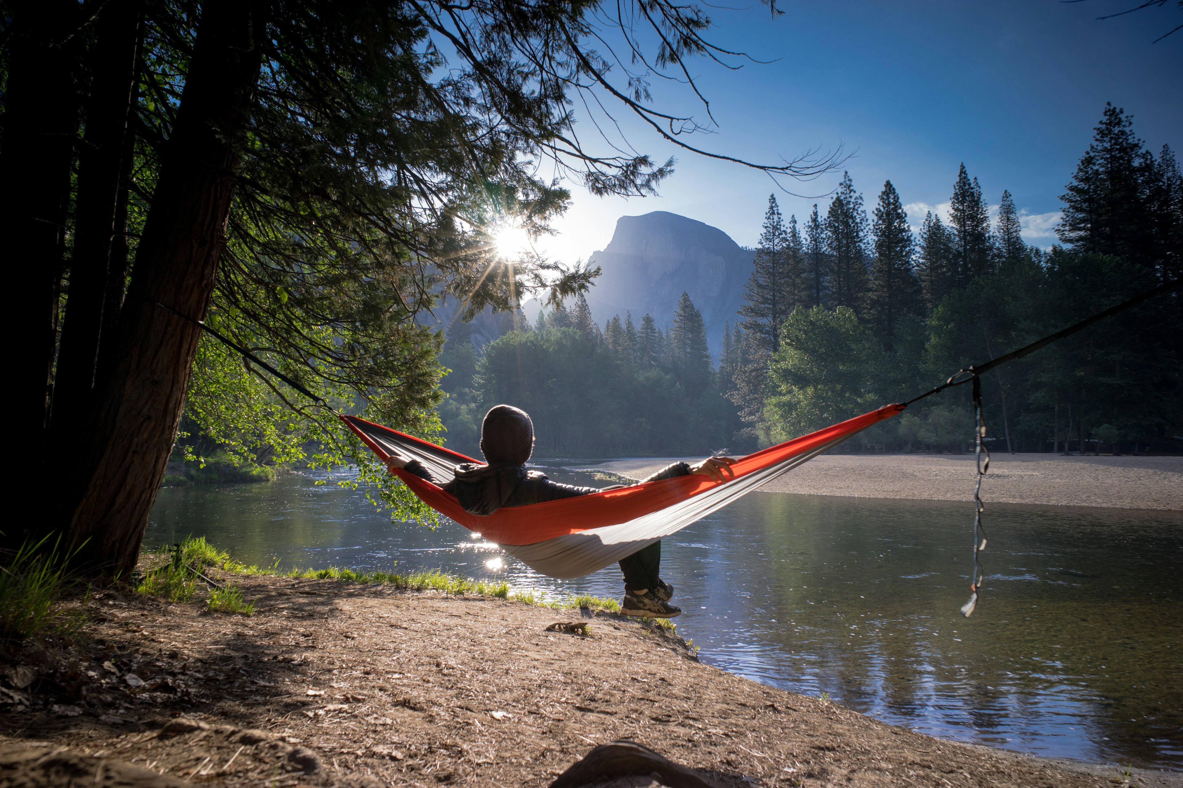 Hiker in a hammock strung between two trees looks out at a lake