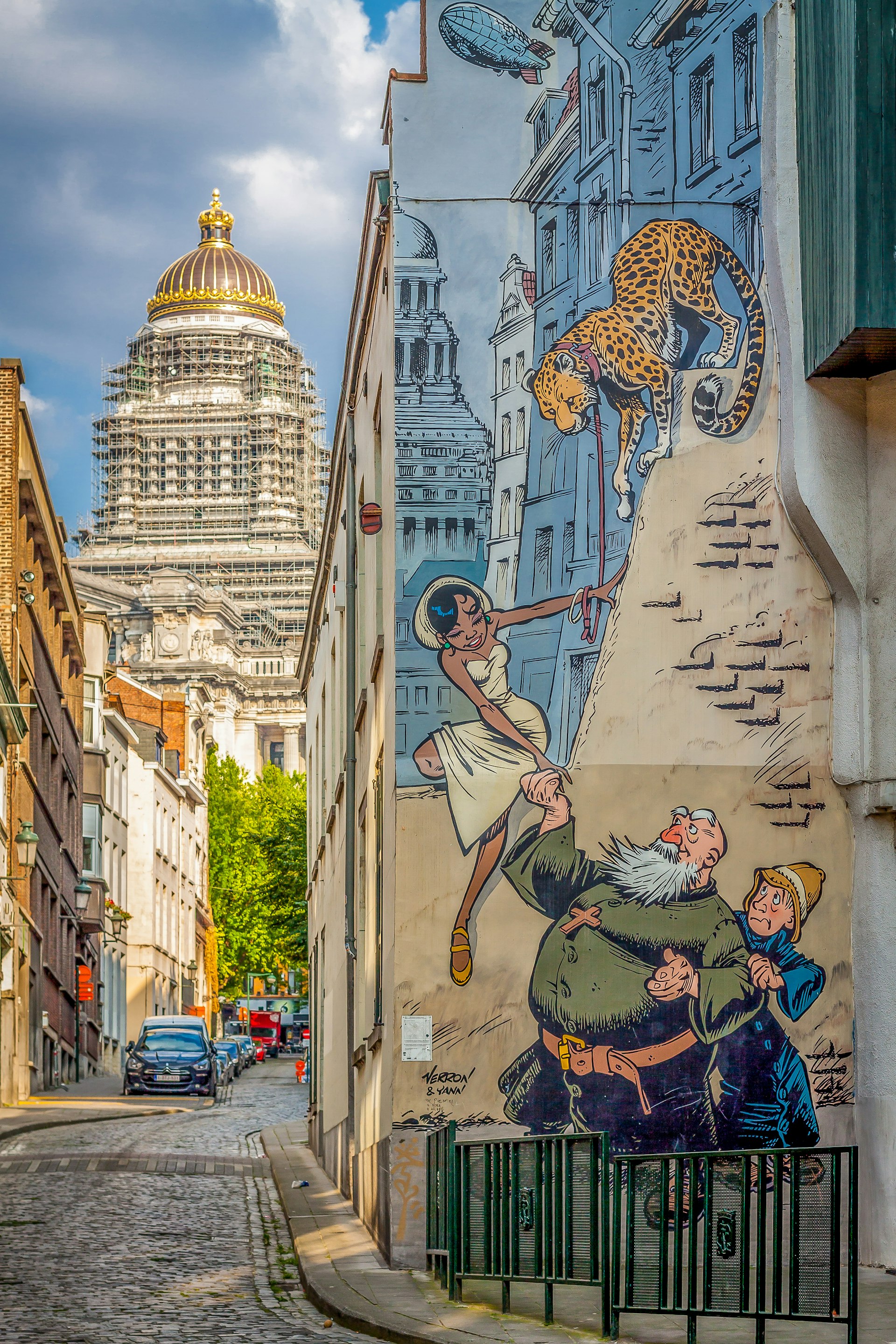 A mural of a comic-book scene covers the entire wall of a traditional house on a narrow cobbled street in Brussels.