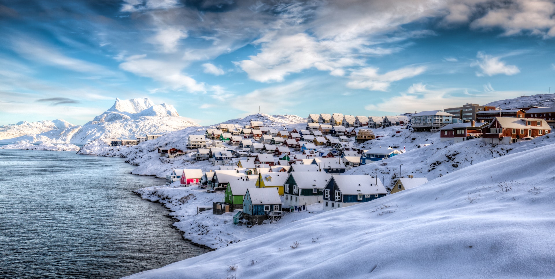 A view of multicolored houses on the snow-covered shore of Nuuk, Greenland, with icy mountains in the background