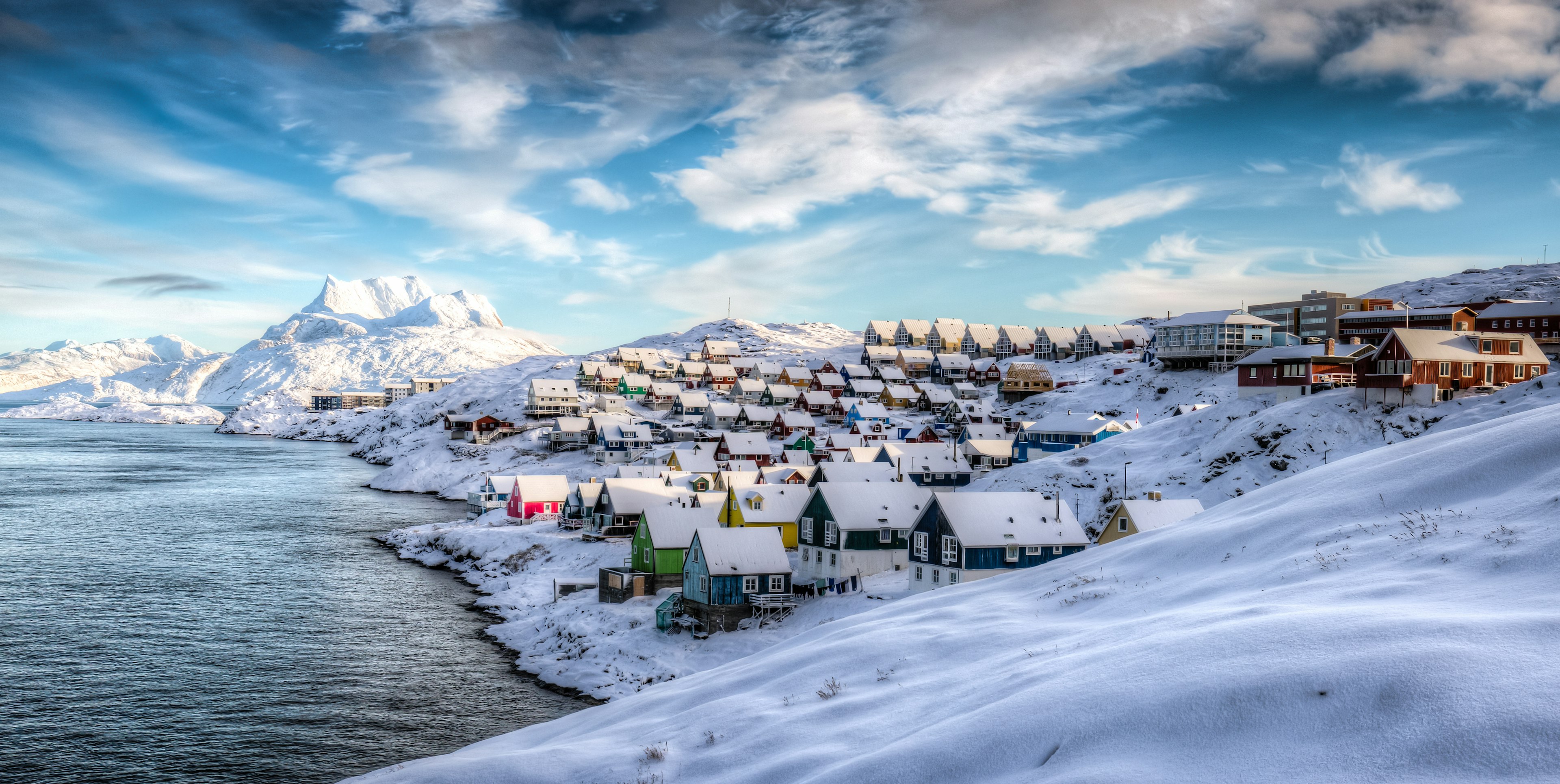 A view of multicolored houses on the snow-covered shore of Nuuk, Greenland, with icy mountains in the background