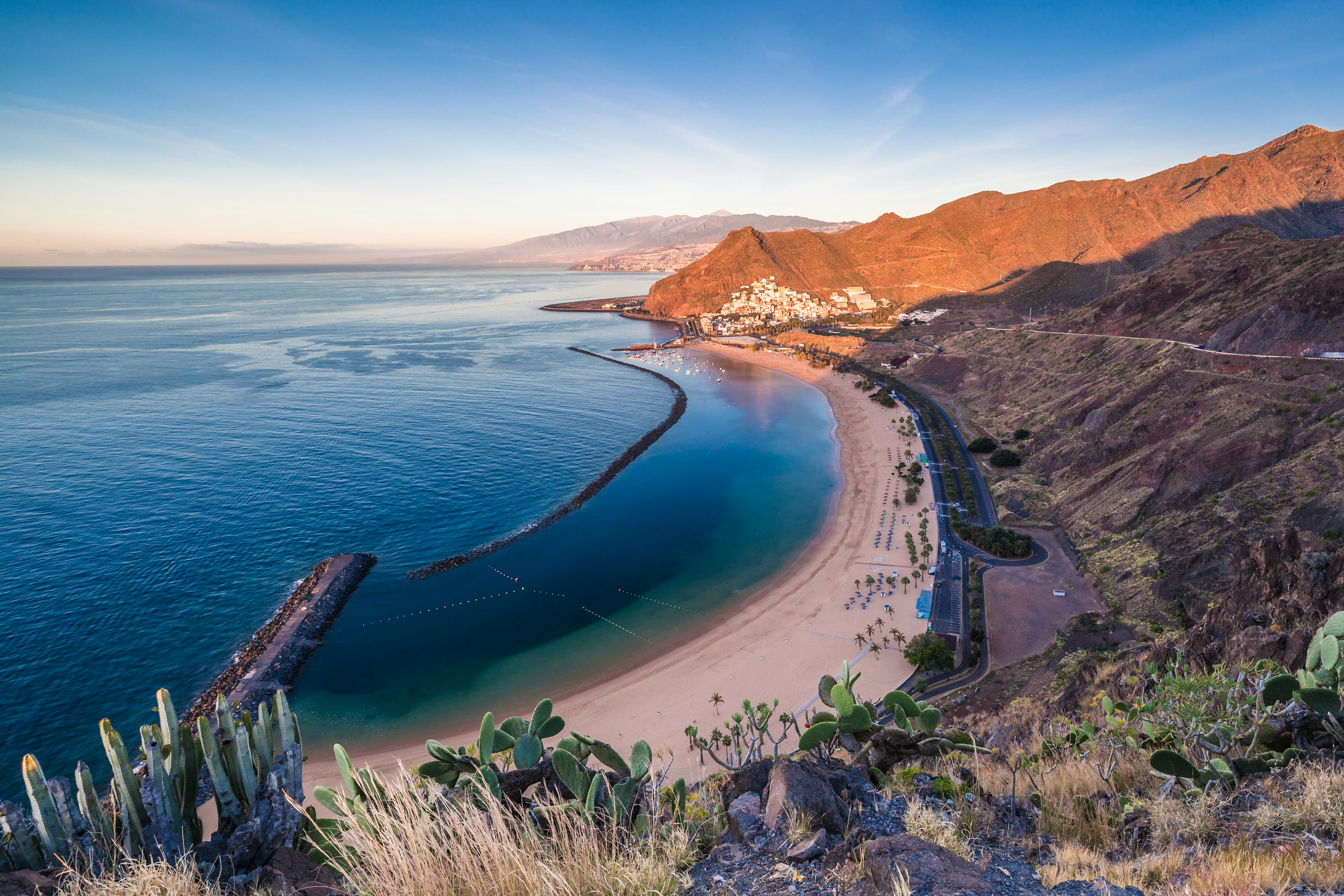 An empty curve of white sand at sunrise. A breakwater separates the ocean from a safe swimming area