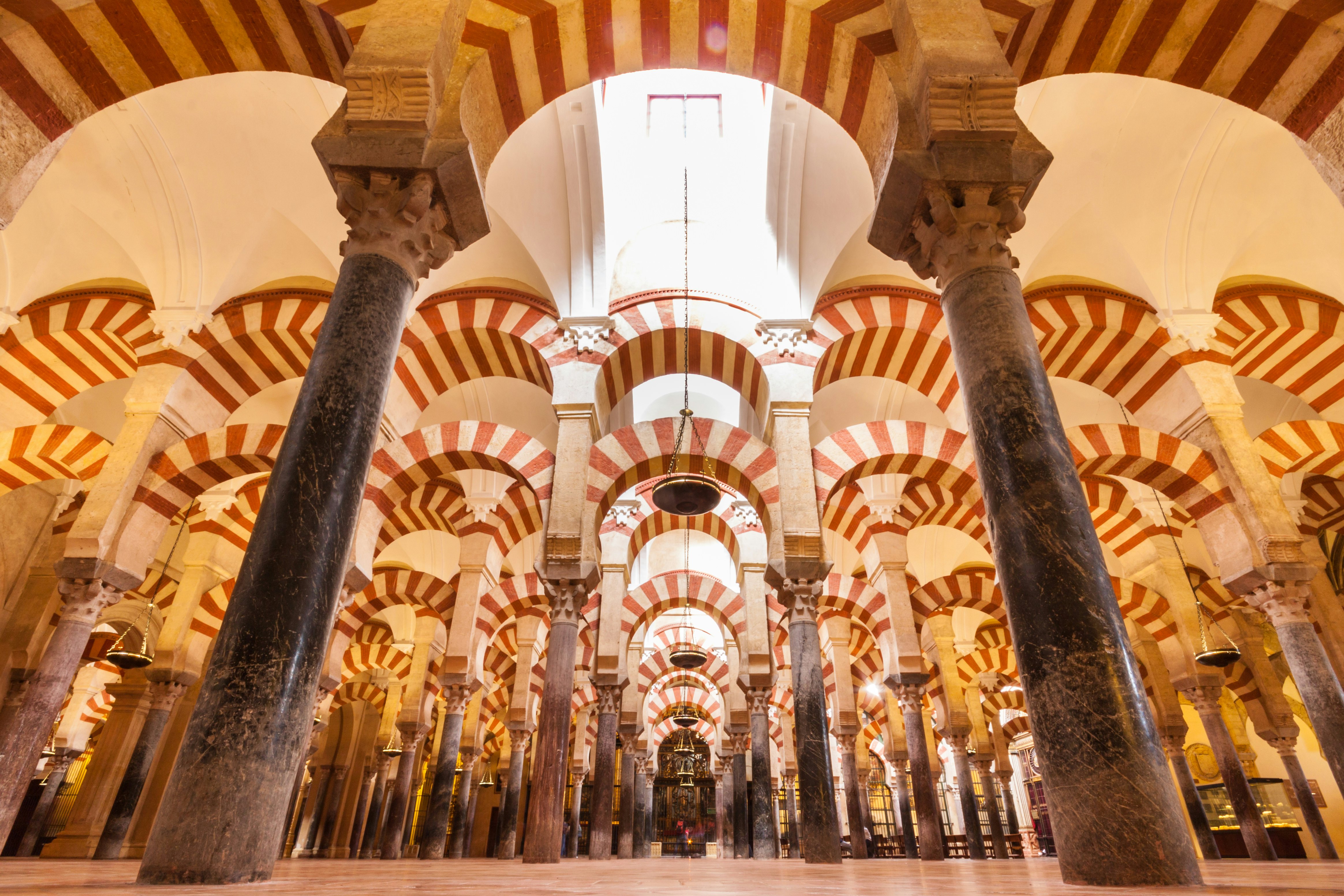 An upwards shot of the interior of a building with many columns and archways, with a symmetrical pattern of bricks alternating between red and white