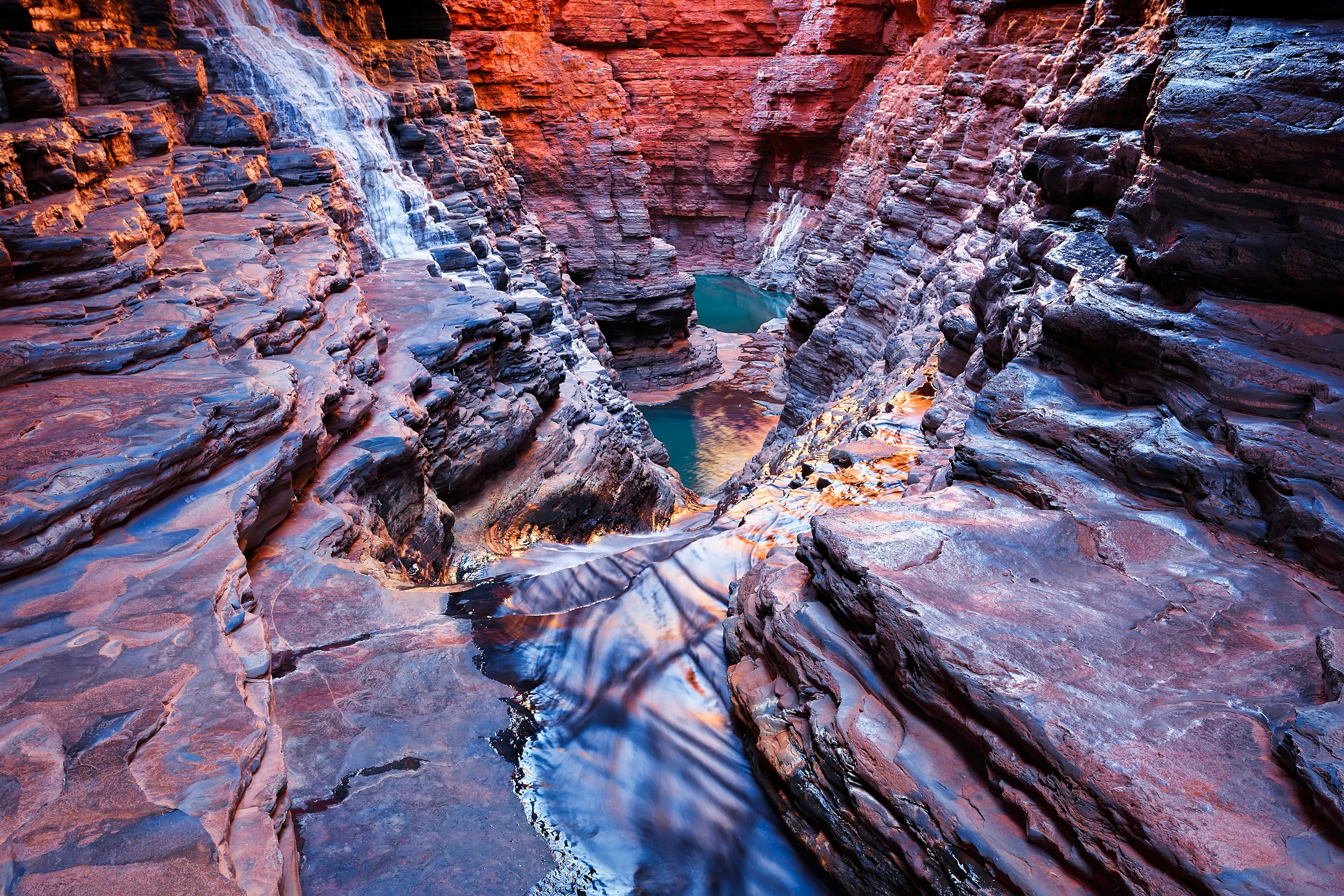 A deep red, layered canyon with rippled sides, as though it's been carved out with water, at Karijini National Park, Australia.