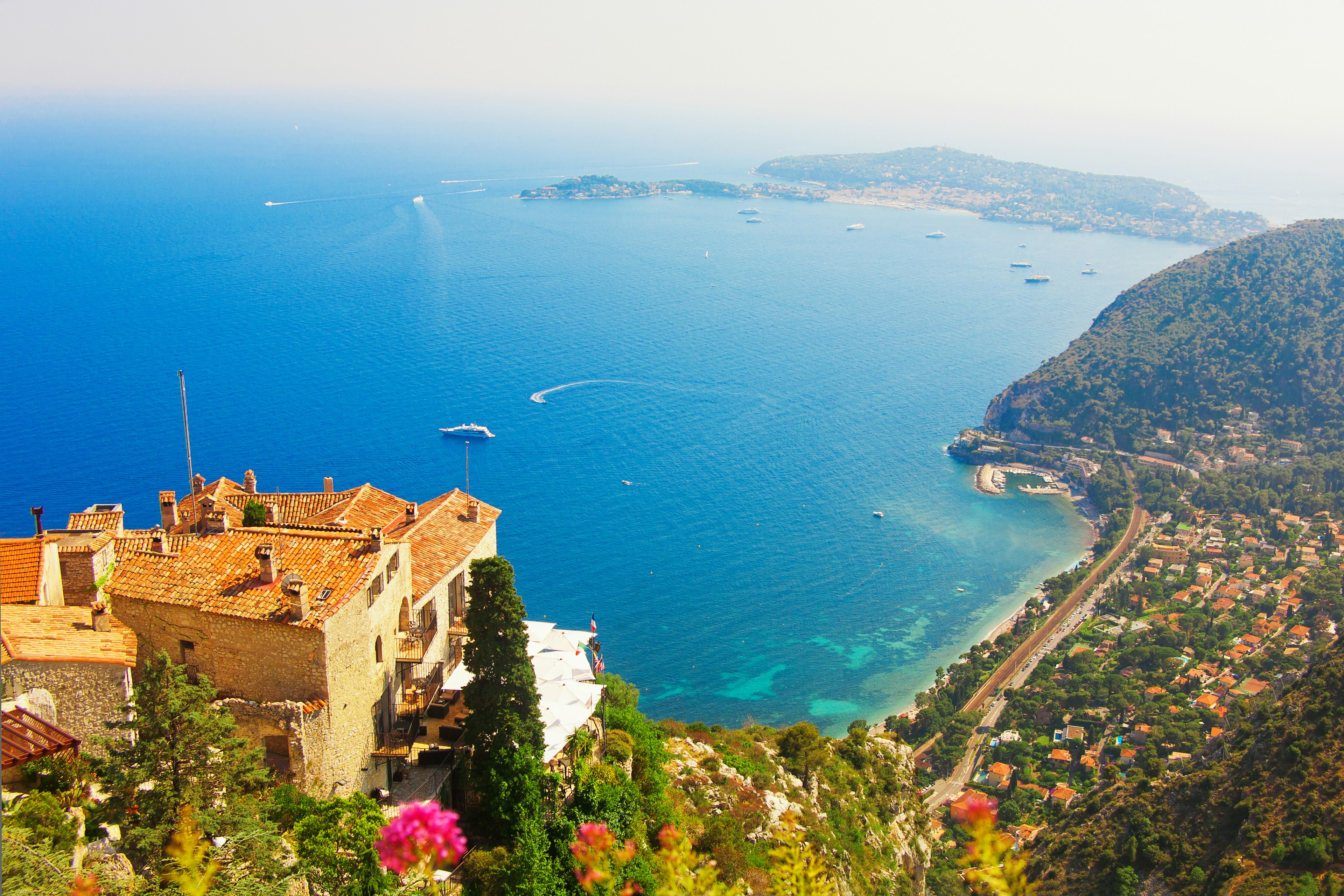 A stone house stands on a hill looking down towards the sea with boats out on the water and the coastline stretching into the distance