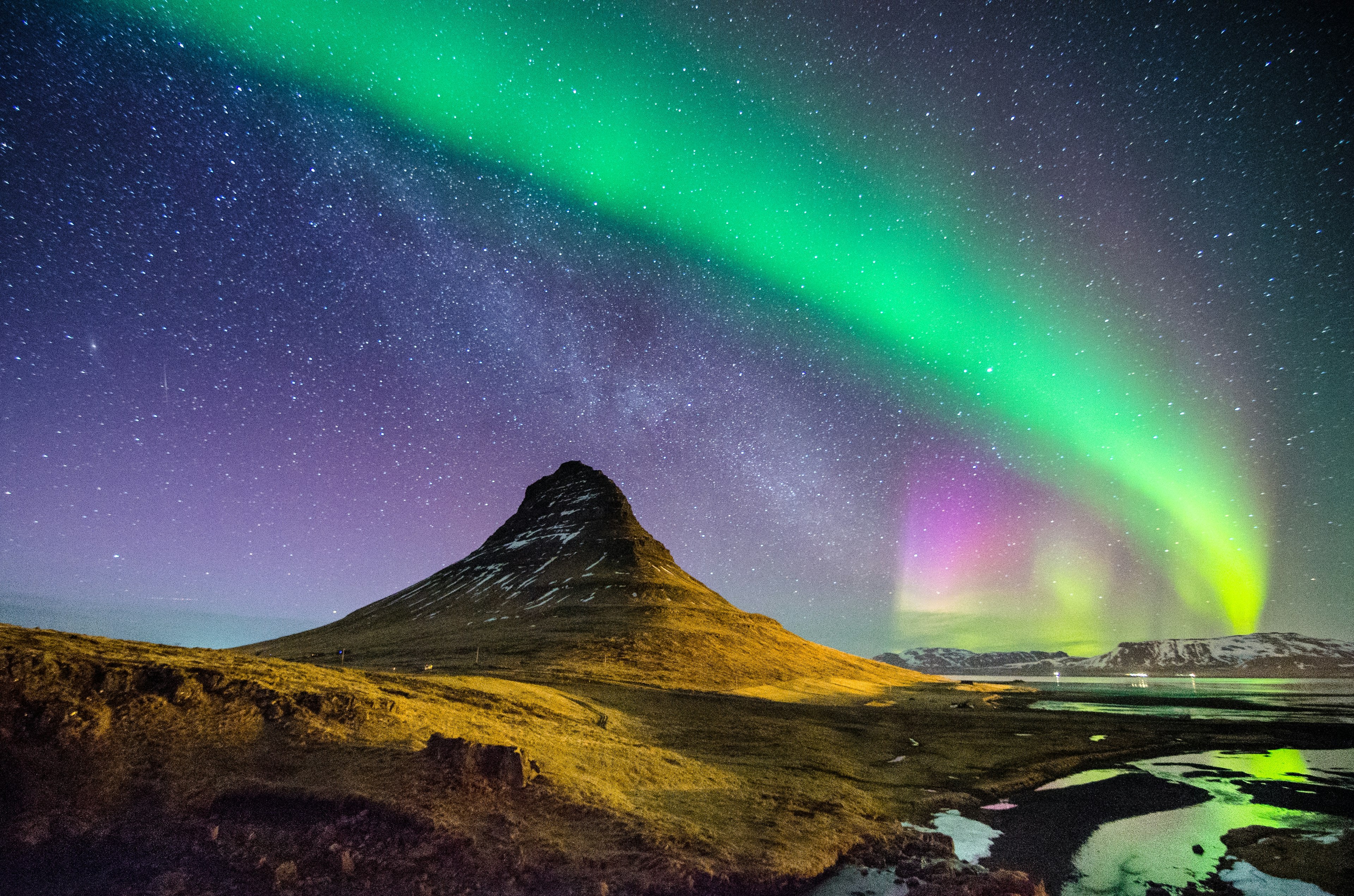 A streak of green and yellow lights sweeps in an arc across the night sky, with millions of twinkling stars shining through.