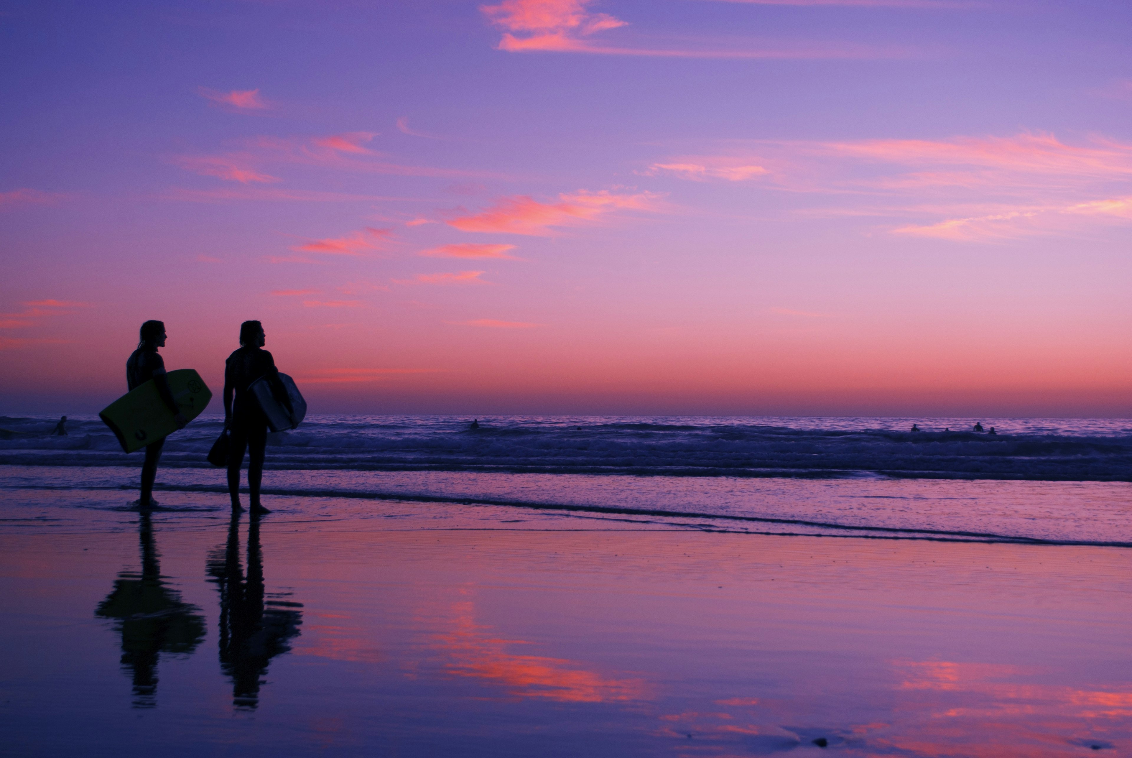 In a swirl of orange and purple as the sun disappears, two silhouettes of surfers stand on Taghazout beach in Morocco and survey the sea