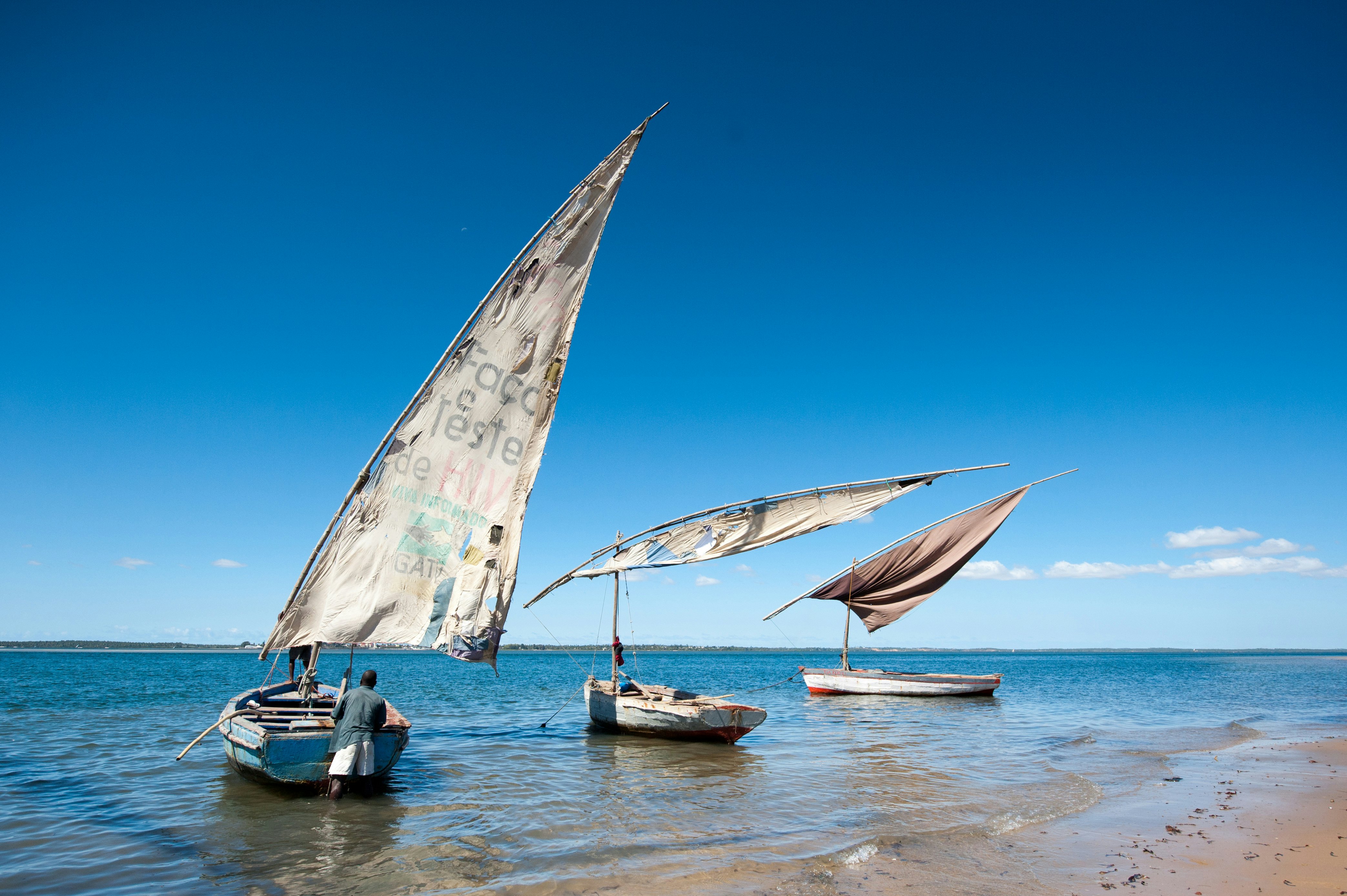 Three small masted boats unfurl their sales on the shores of Lake Malawi